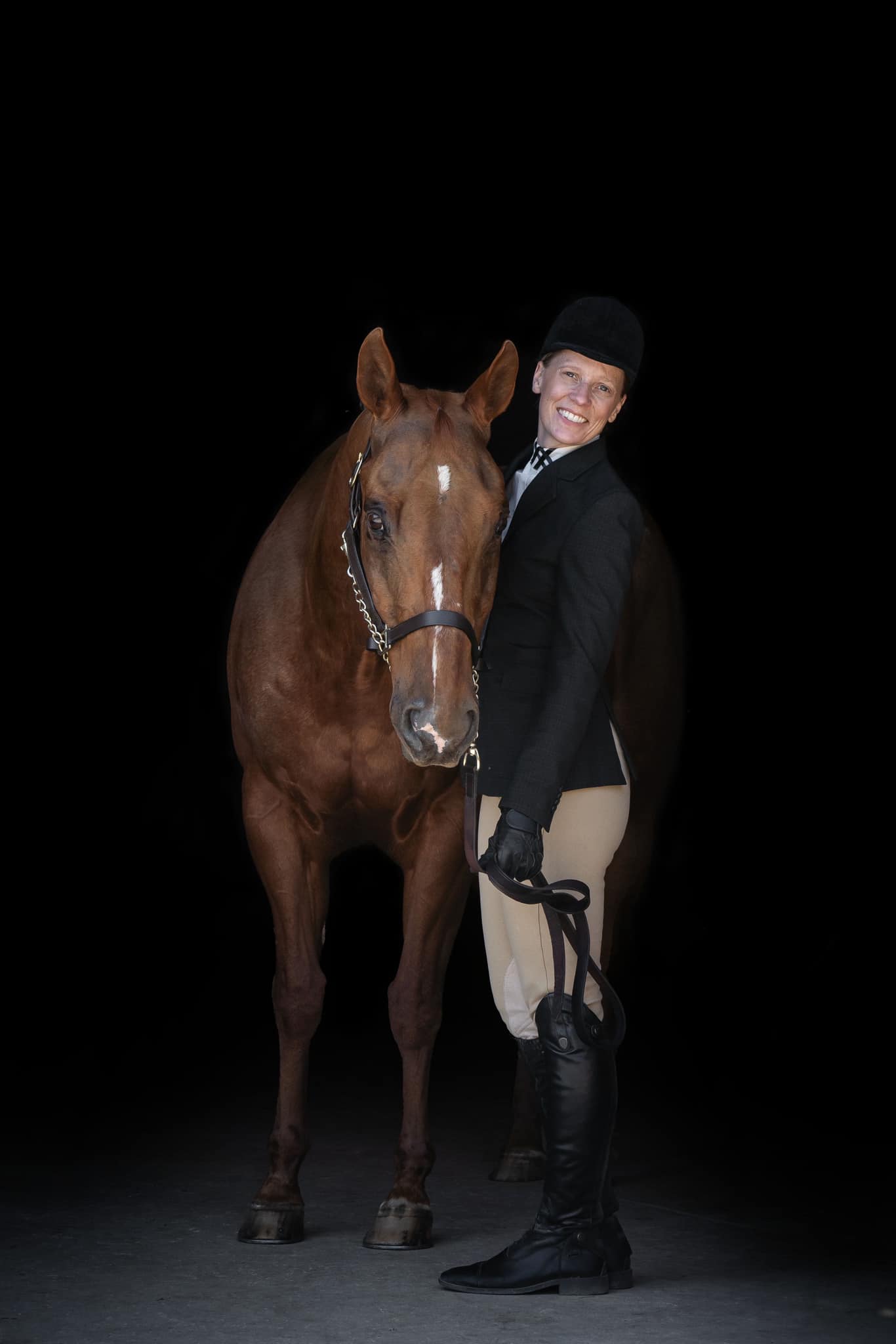 Person standing next to a brown horse, both facing forward, against a black background.