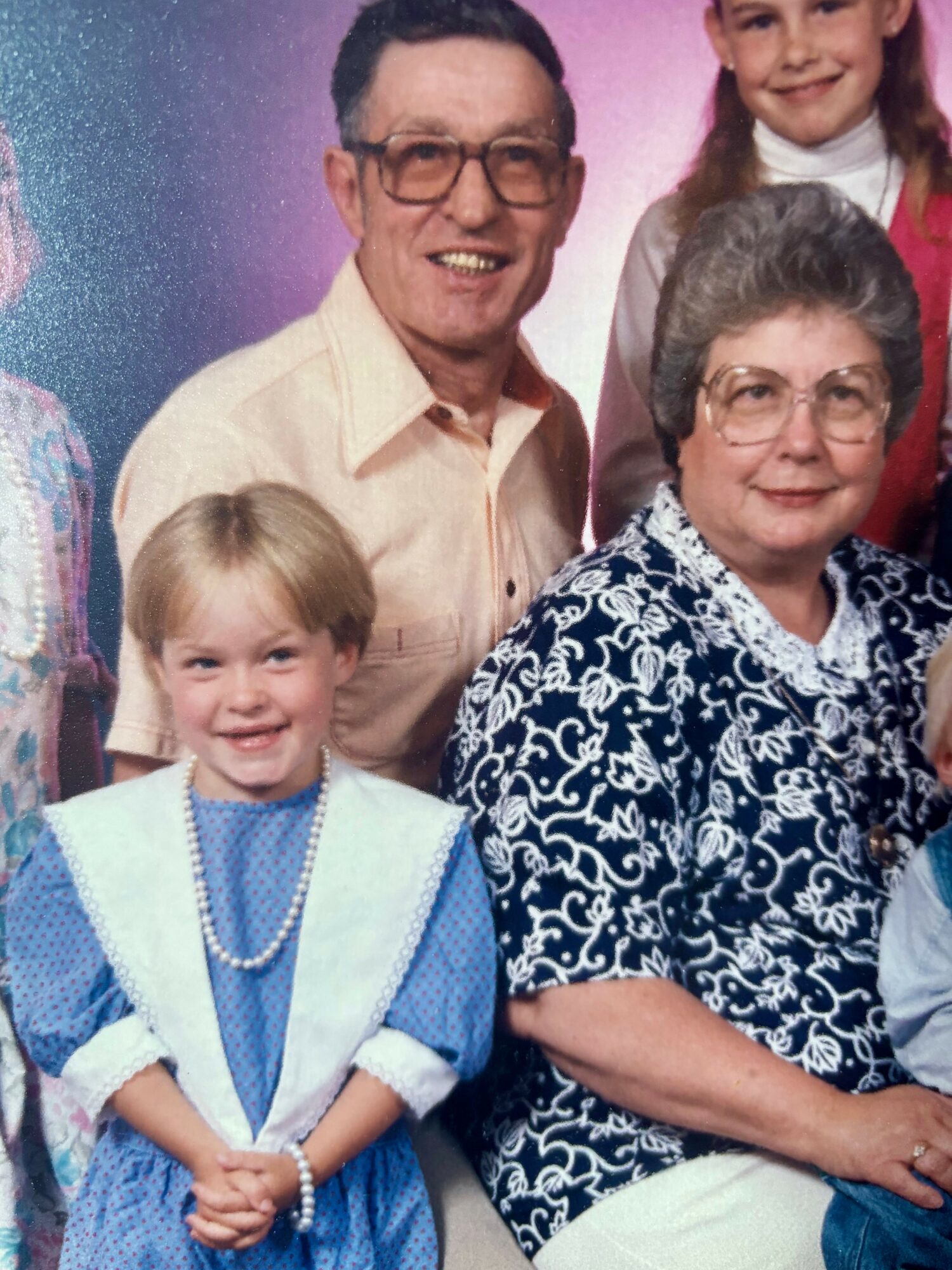 Group of people, including a young girl in a blue dress, an older woman, and a man, smiling together.