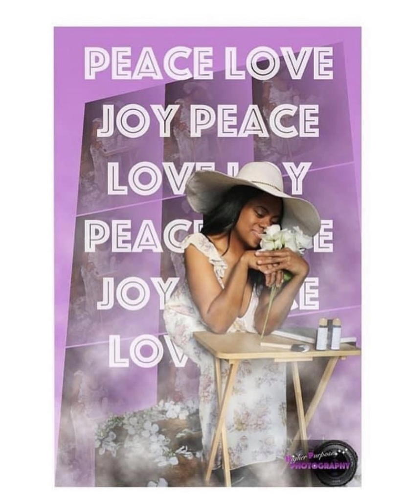 Woman with a hat holding a flower, sitting at a table with a purple background and words like PEACE, LOVE, JOY.