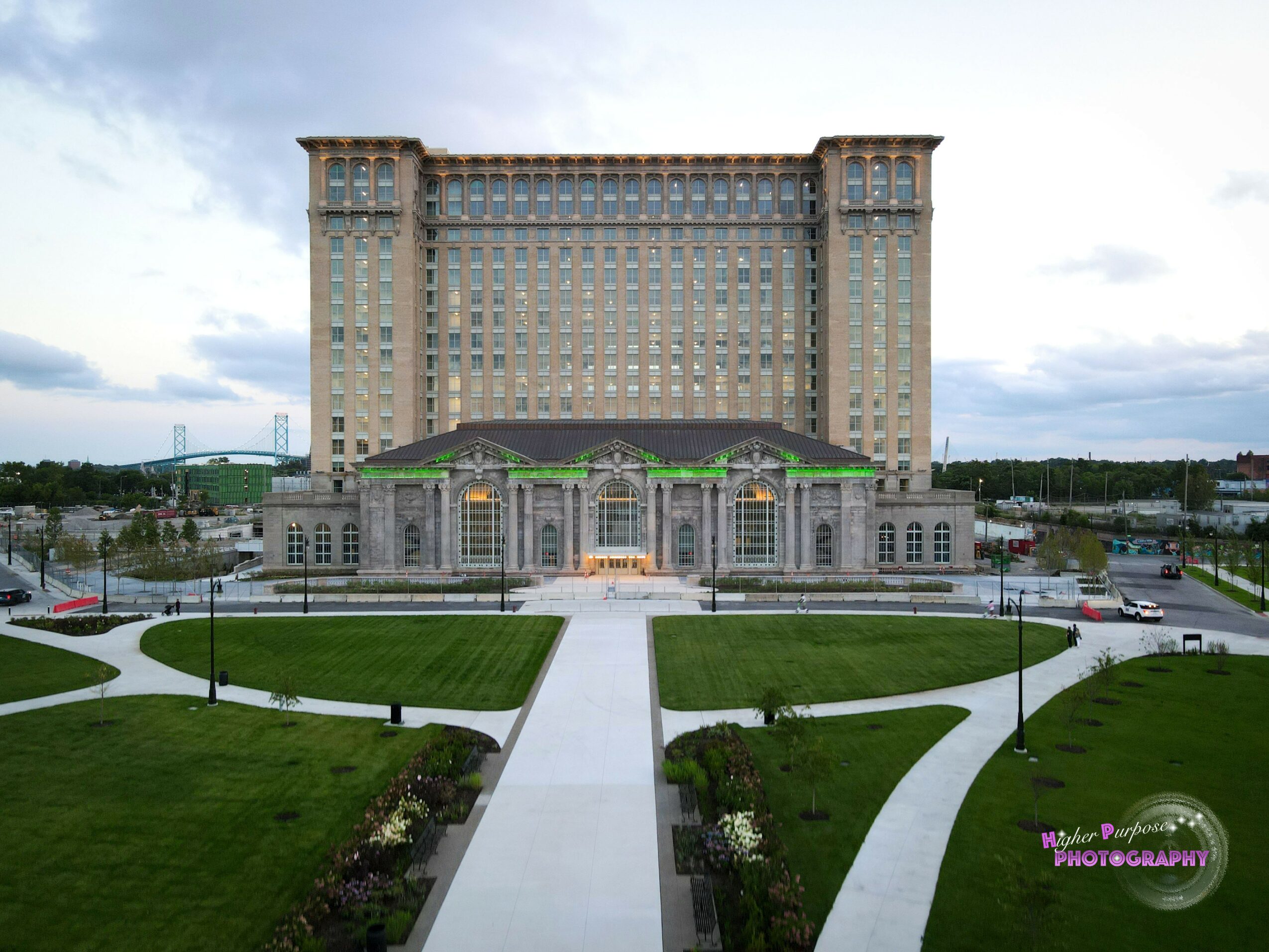 Large hotel building with a grand entrance, surrounded by green lawns and pathways, under a cloudy sky.