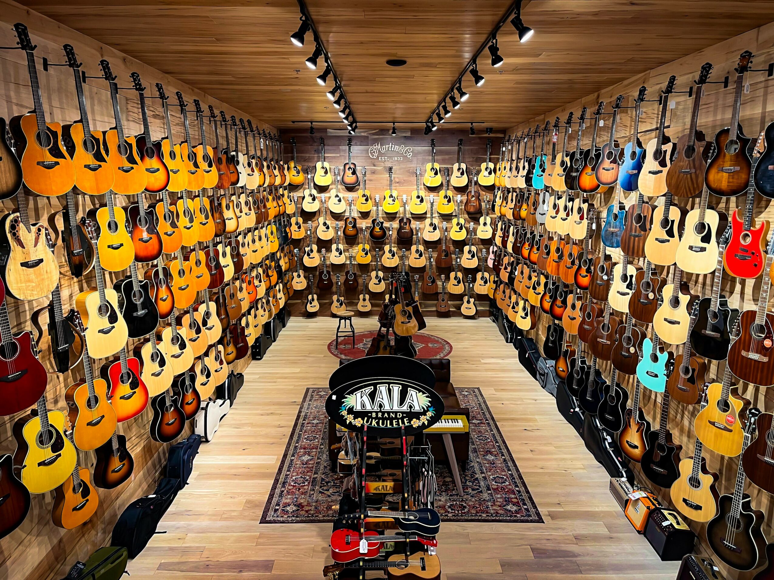 Room filled with guitars hanging on walls, arranged by color and style, with a central display and a rug on wooden floor.