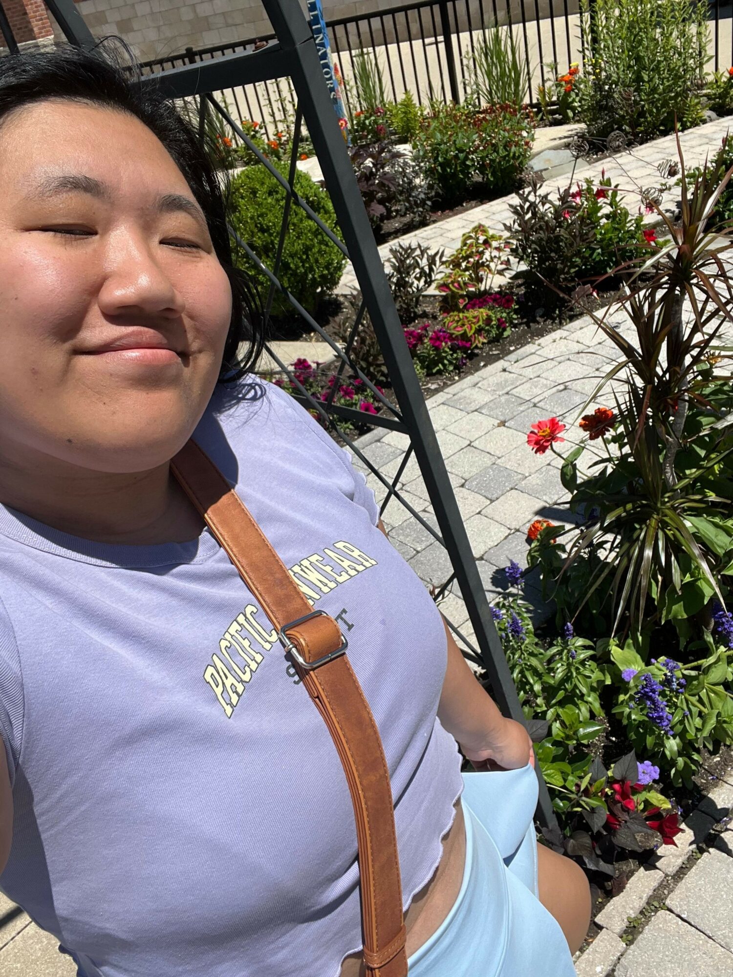 Person taking a selfie outdoors with colorful flowers and plants in the background.