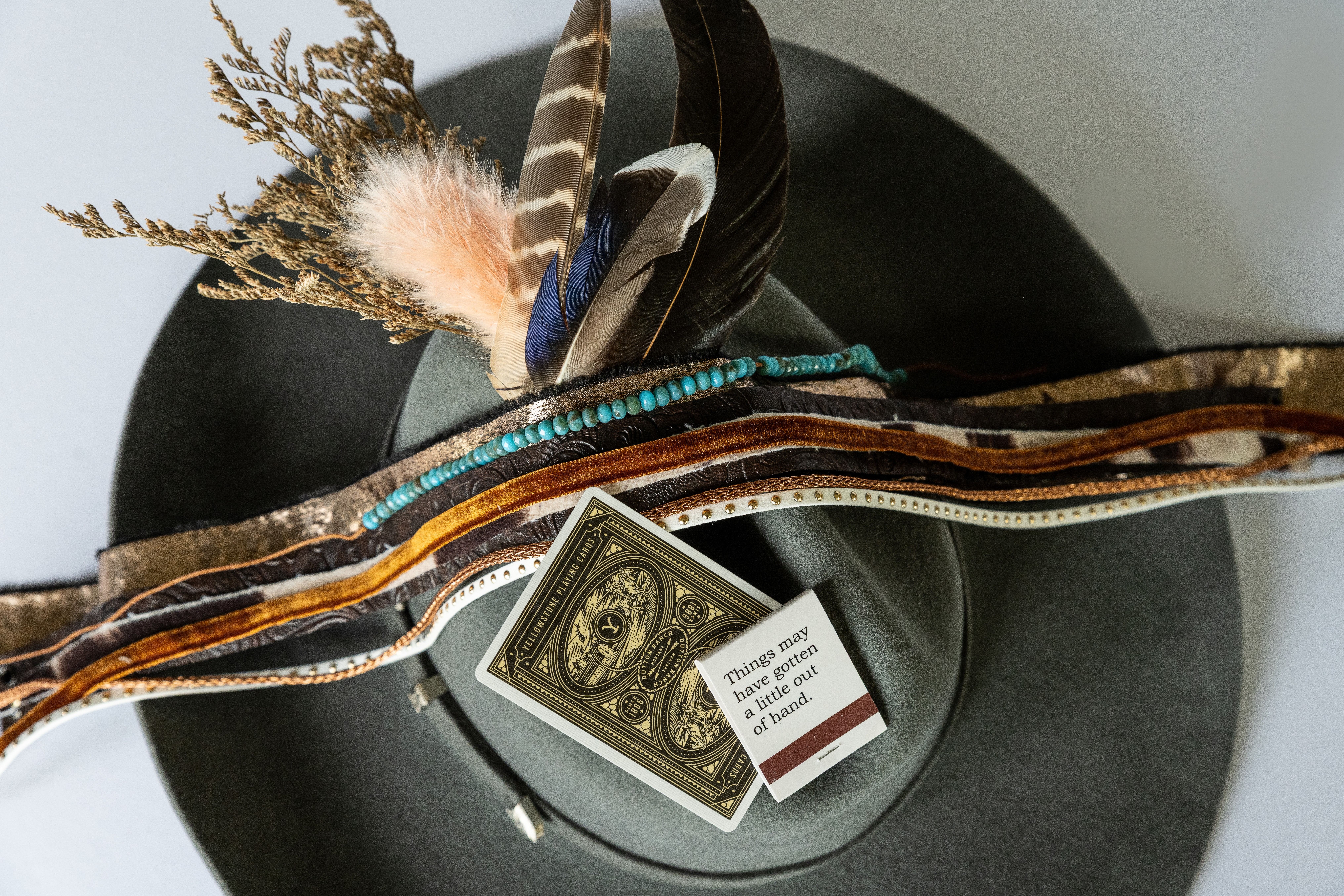 Hat decorated with feathers, dried plants, and a dollar bill, placed on a black surface.