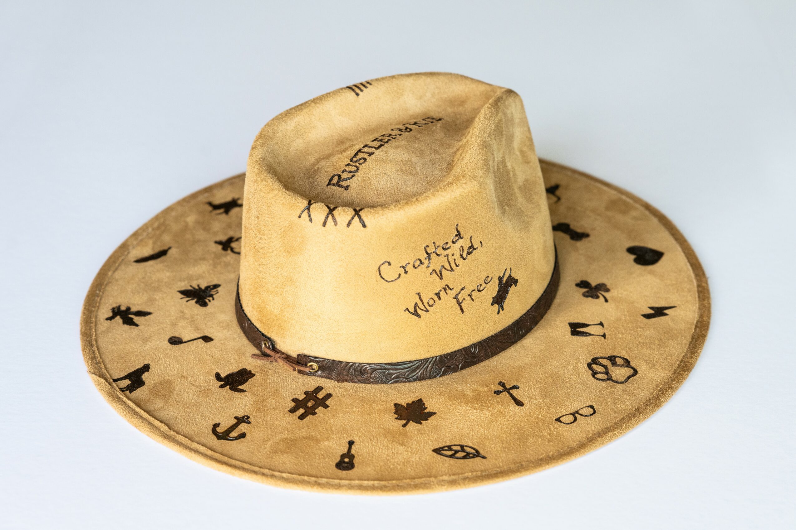 A beige cowboy hat with black symbols and text, featuring a wide brim and a tall, creased crown.
