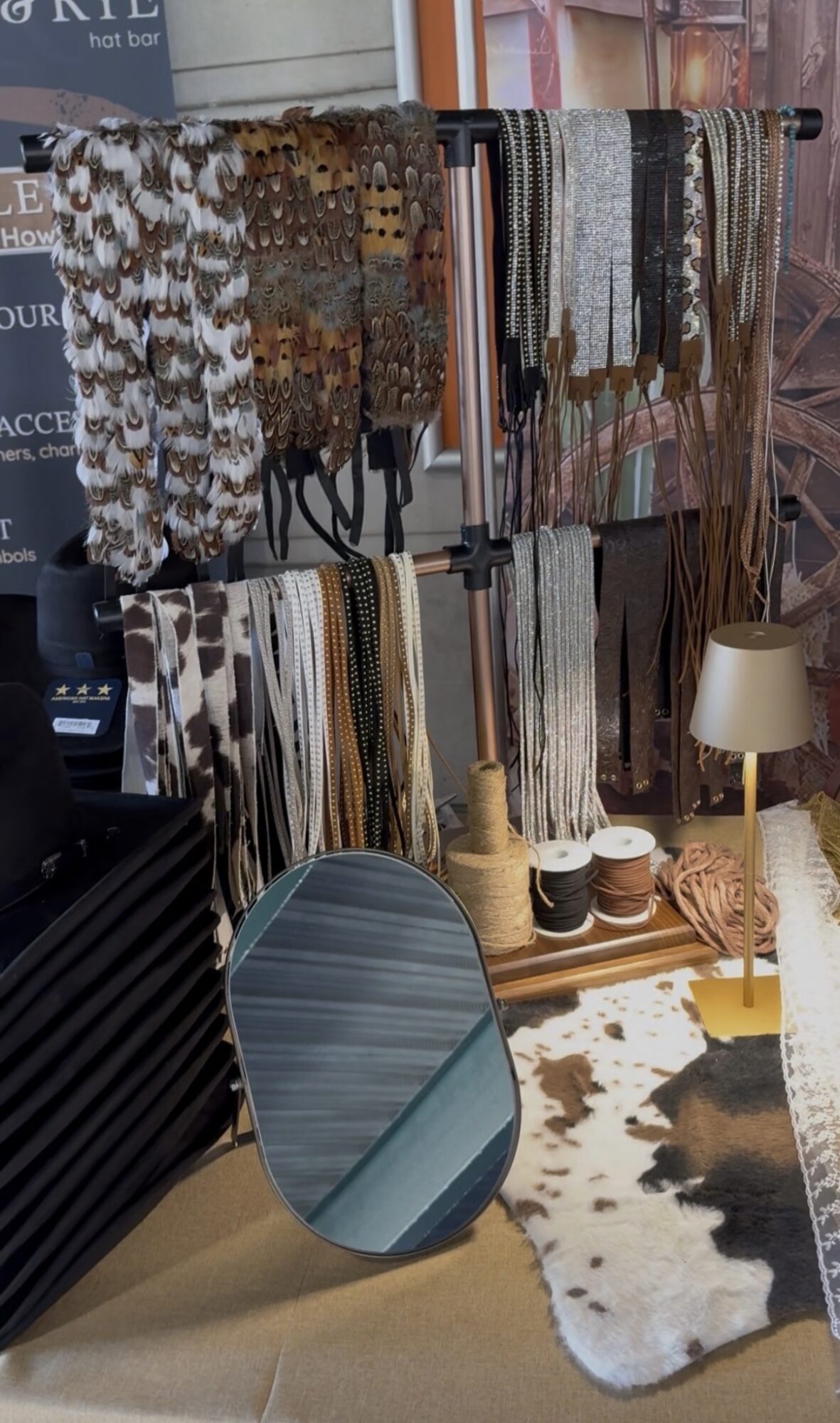 Display of fabric samples hanging on rods, a round mirror, a lamp, and a cowhide rug on the floor.