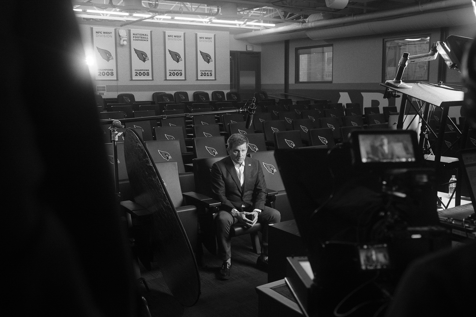 Man in suit sitting in an empty conference room with cameras and equipment around him.
