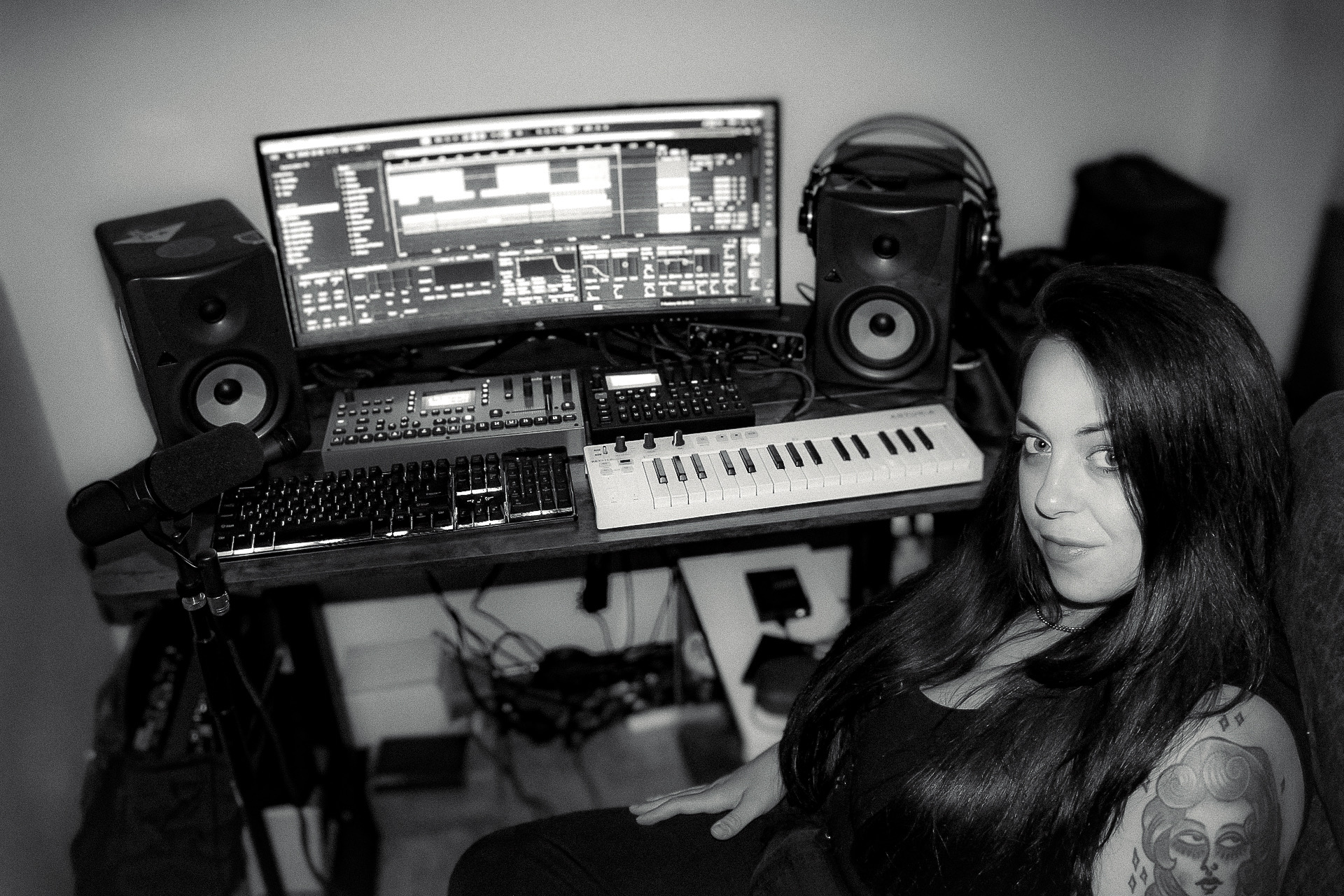 Woman with long dark hair sitting in a music studio with a computer, speakers, and musical equipment.