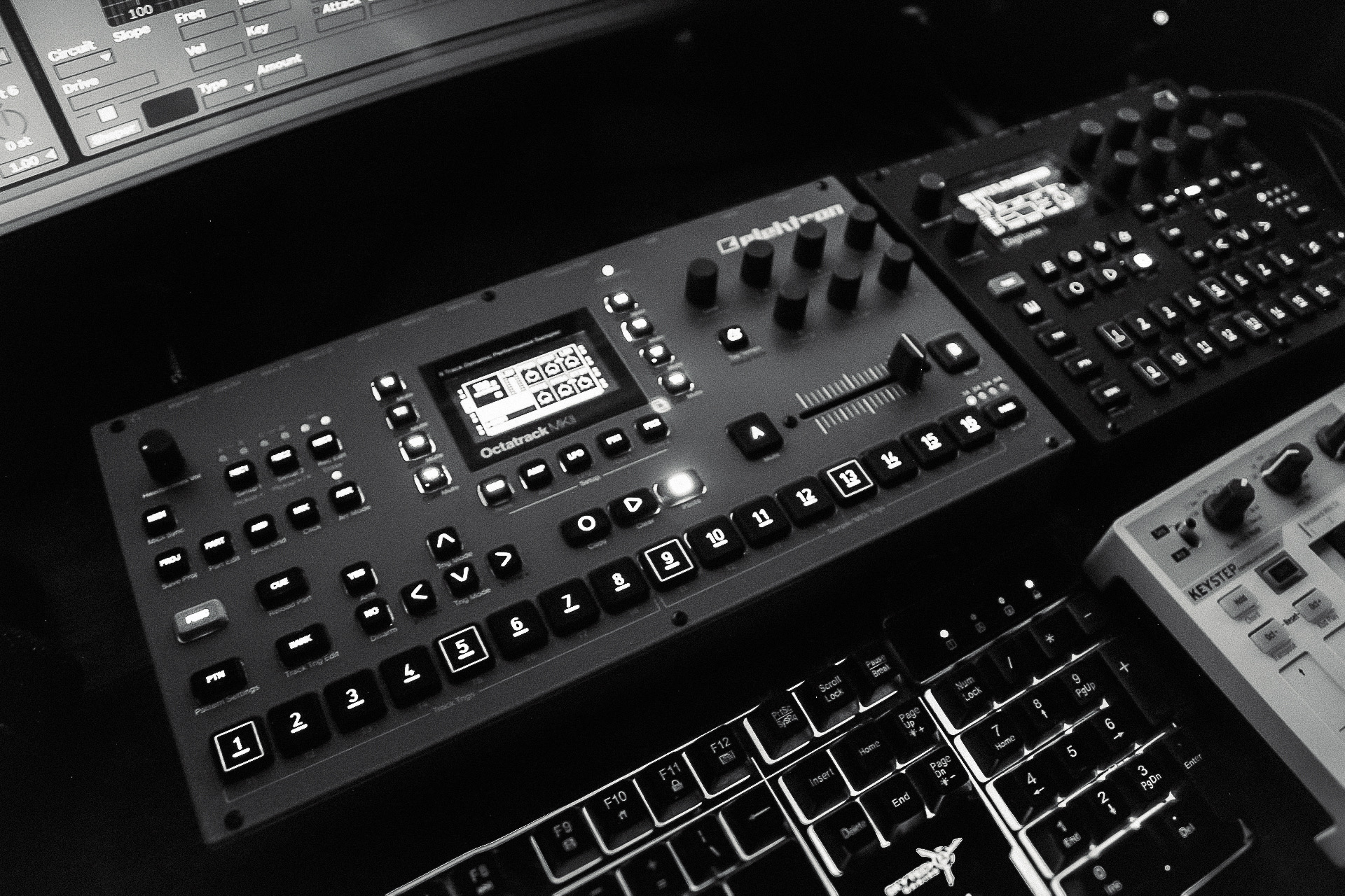 Black music production equipment with buttons, knobs, and screens on a desk, in a studio setting.