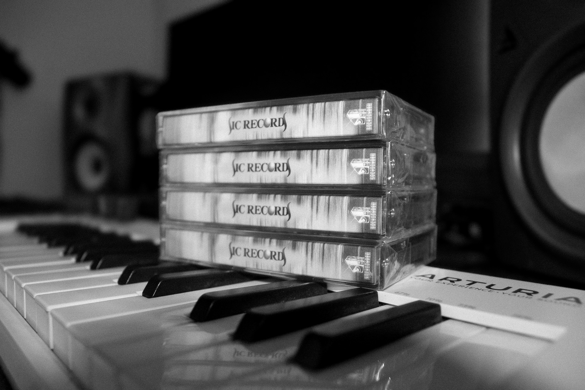 Stack of five cassette tapes on a piano keyboard with speakers in background.