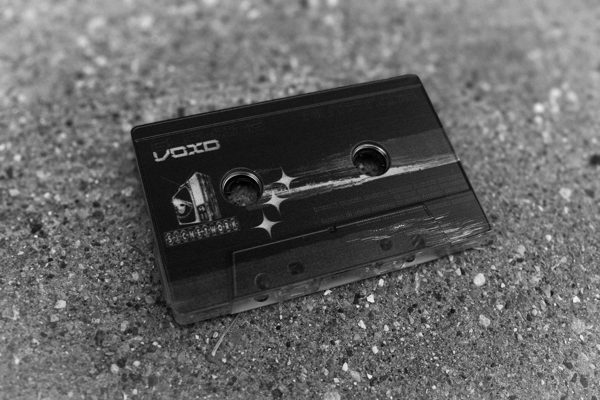 A black cassette tape lies on a textured surface, with visible spools and label details.