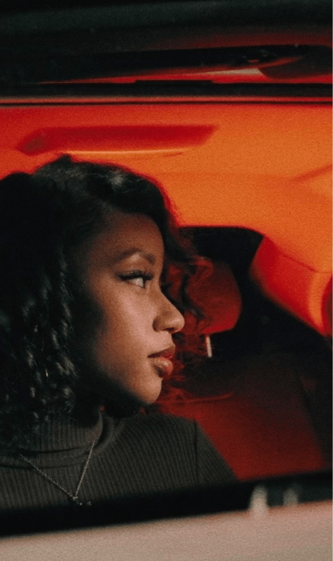 Side profile of a woman with curly hair inside a car with red interior lighting