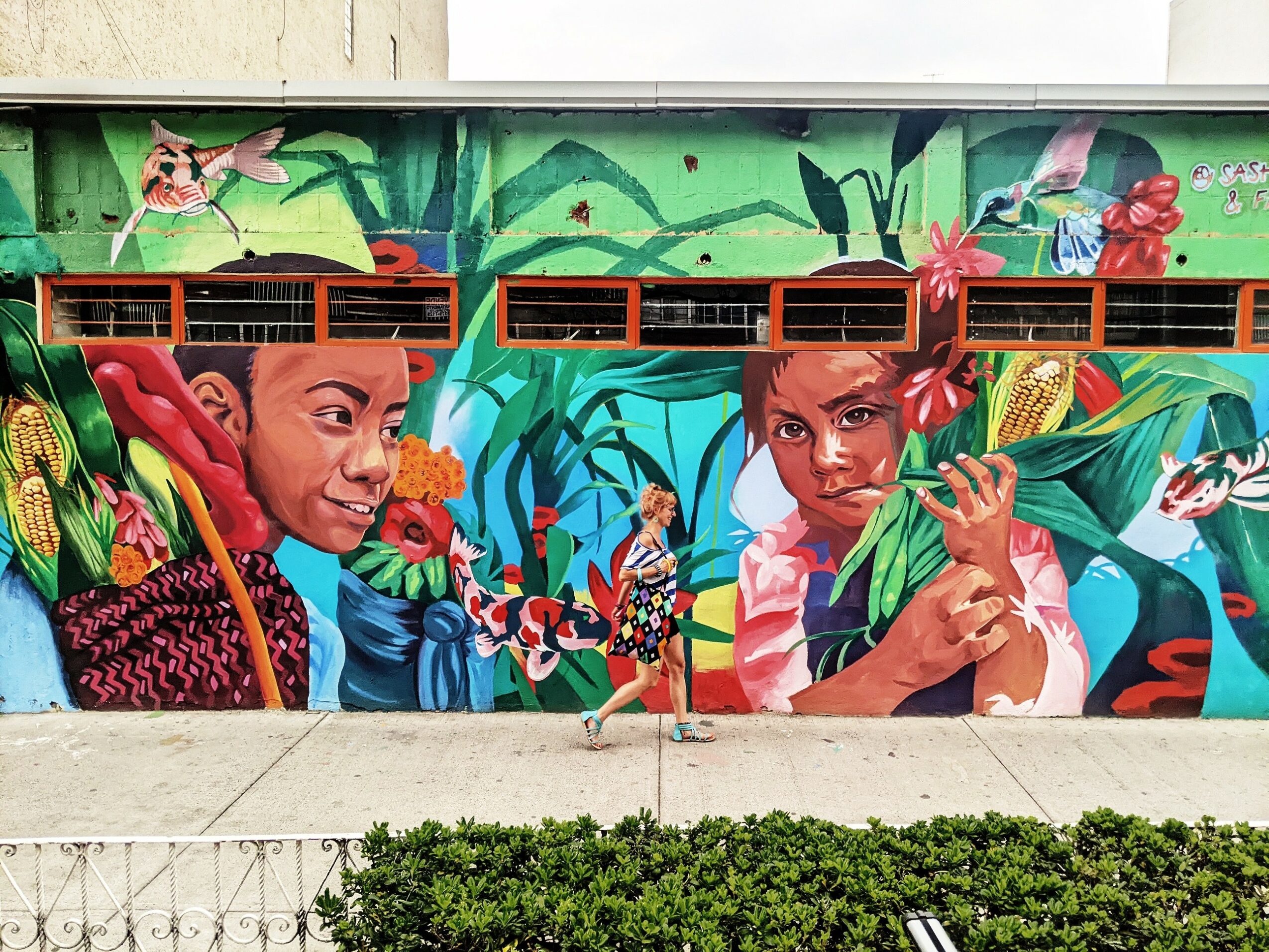 Colorful mural of two children with butterflies and flowers, vibrant green background, detailed and lively scene.