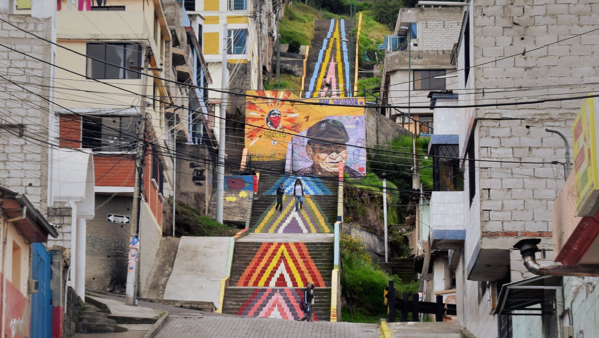 Colorful mural of a person wearing sunglasses on a city street with buildings and stairs in the background.