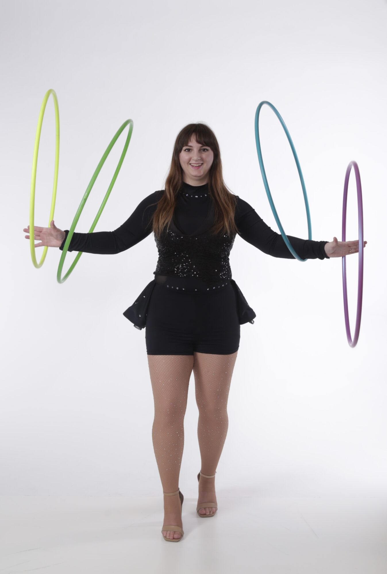 Woman in black outfit holding colorful hoops, smiling, standing on a white background.