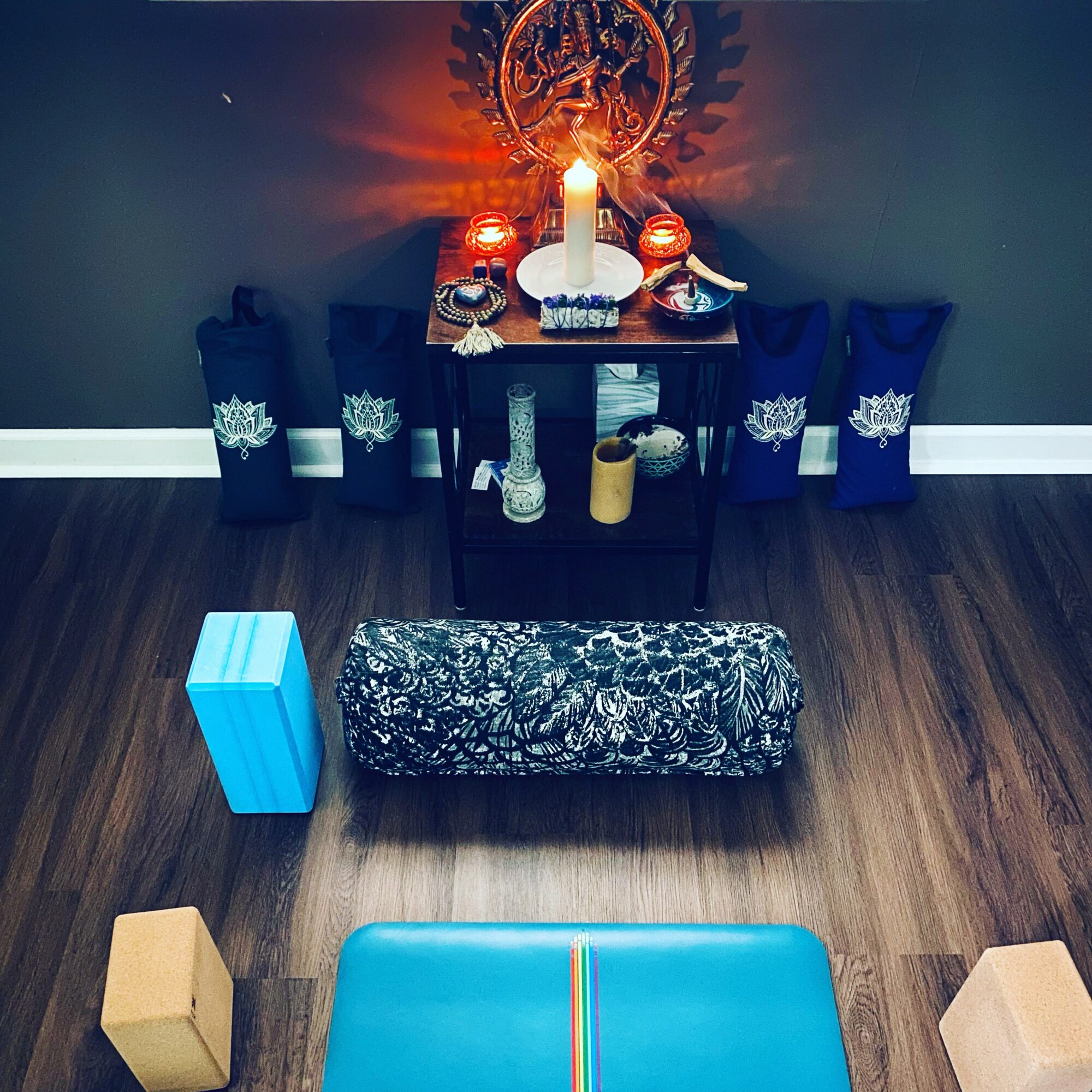 Altar with candles, decorative items, and a spiritual symbol, surrounded by chairs and objects on a wooden floor.