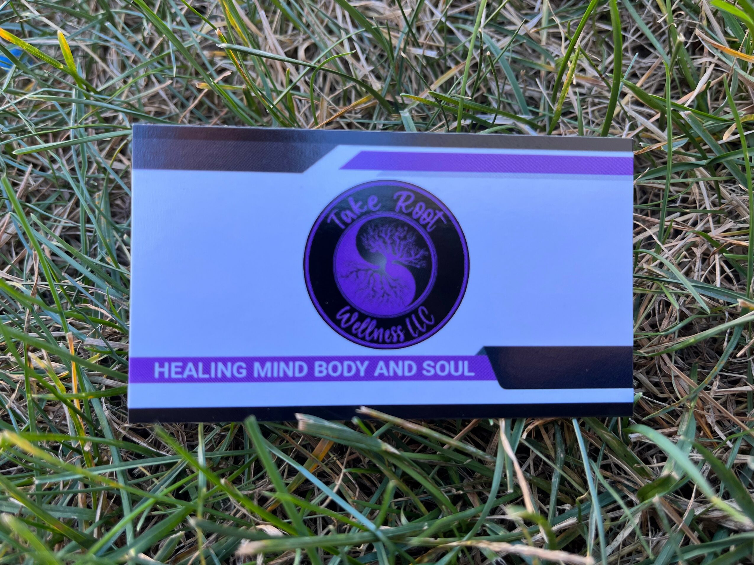 Business card with purple and black logo, text reads 'The Real Outlaw' and 'Healing mind body and soul', on grass