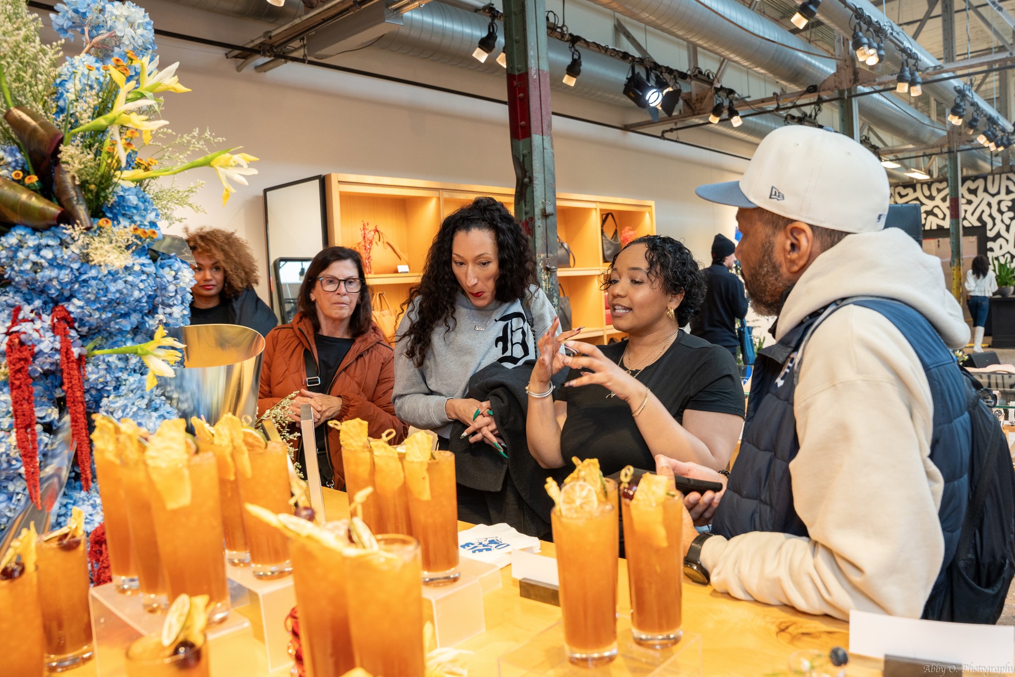 Group of people gathered around a table with orange drinks, decorated with a Christmas tree, in an indoor setting.
