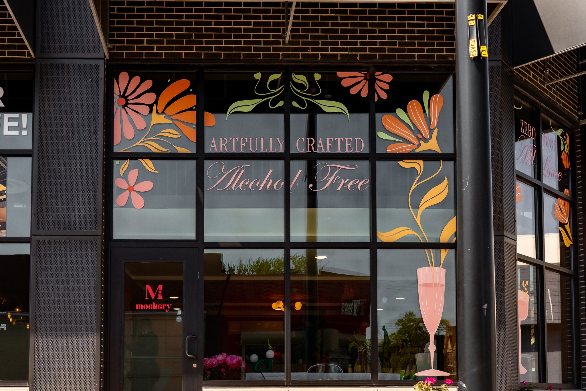 Storefront with floral artwork and sign reading 'Artfully Crafted' and 'Macher Tree', glass windows reflect outdoor scene.