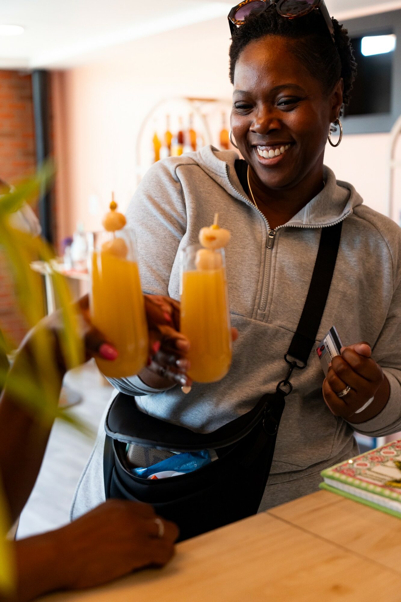 Smiling woman holding a yellow drink with a small umbrella, in a bright indoor setting.