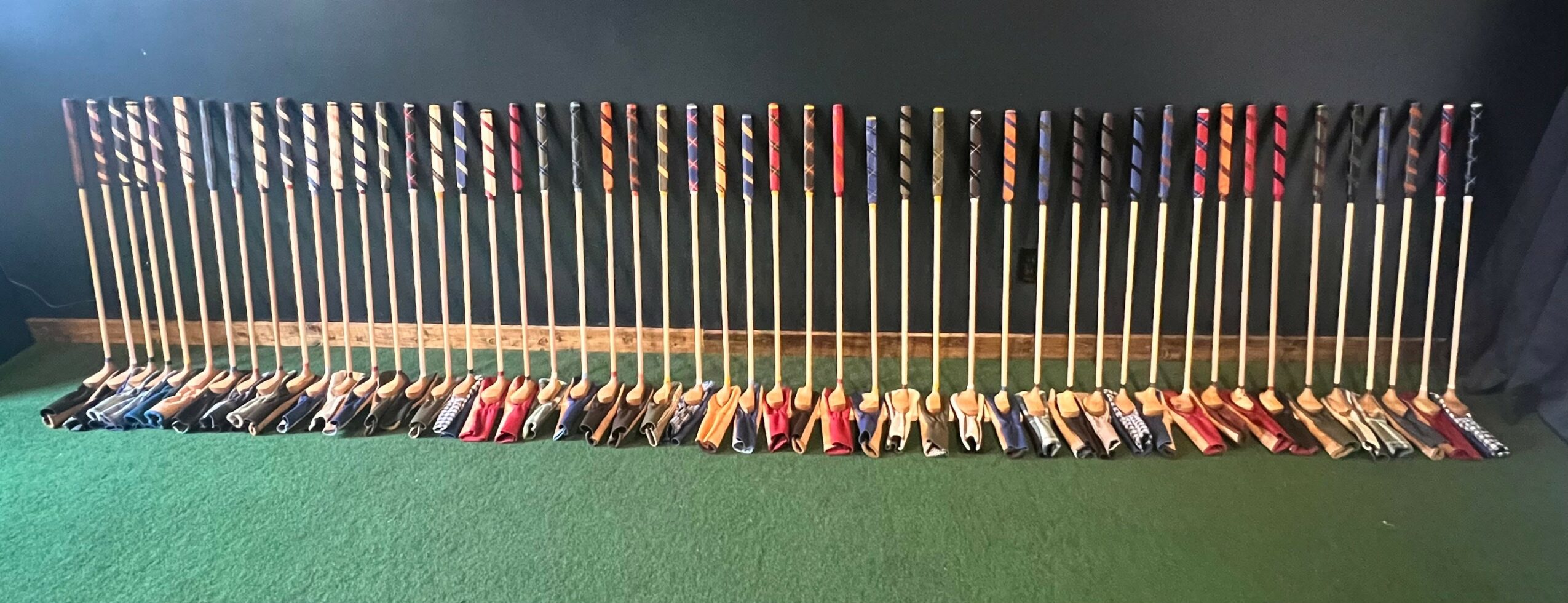 Collection of golf clubs arranged in a row on a green surface, with a dark background.