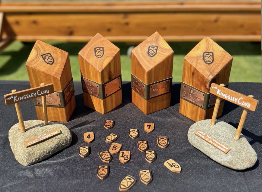 Four wooden blocks with shields, two rocks with signs, and scattered wooden tokens on a black surface, outdoors.