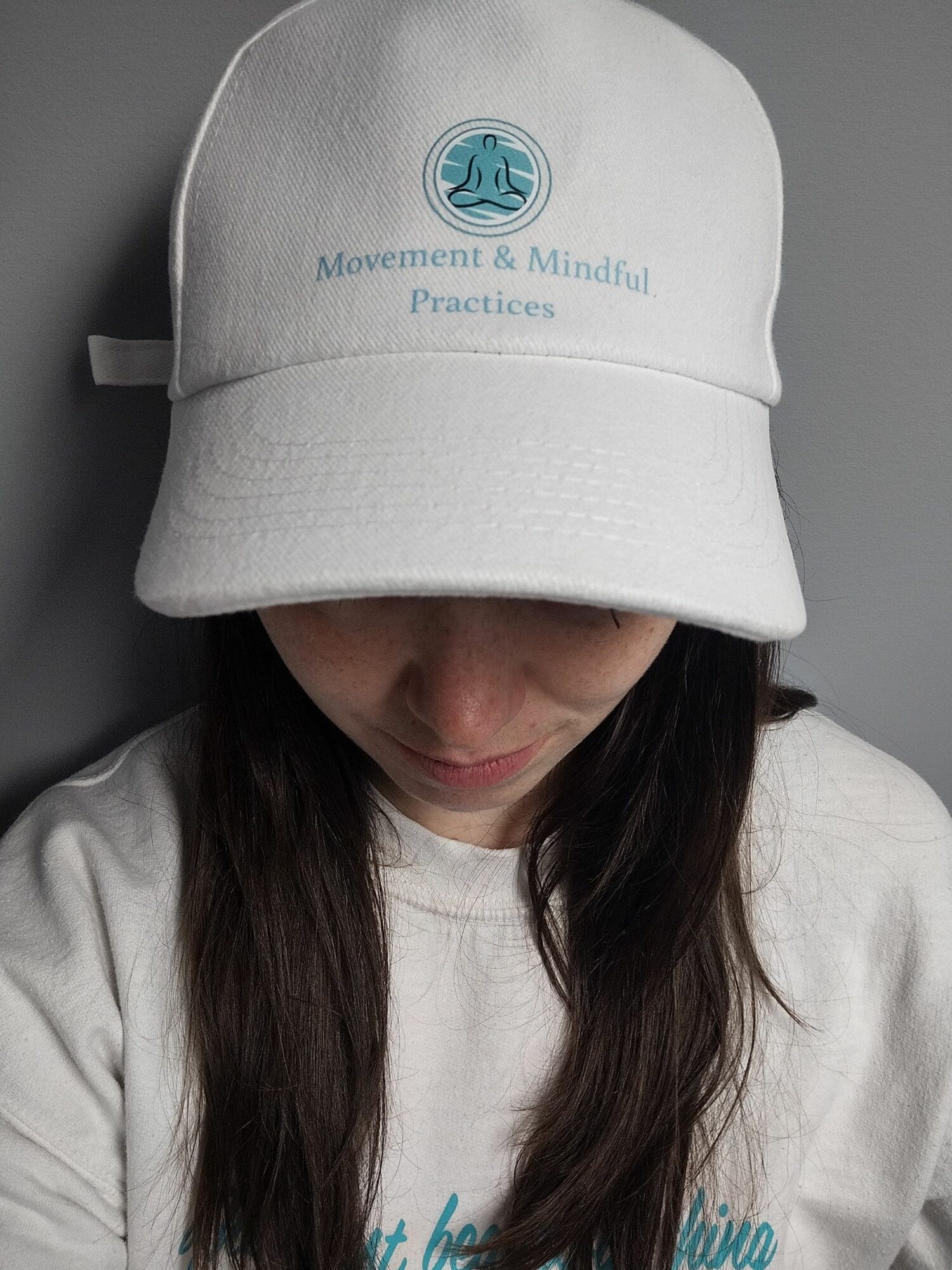 Person wearing a white cap with a logo, partially covering their face, with dark hair visible, in a close-up shot.