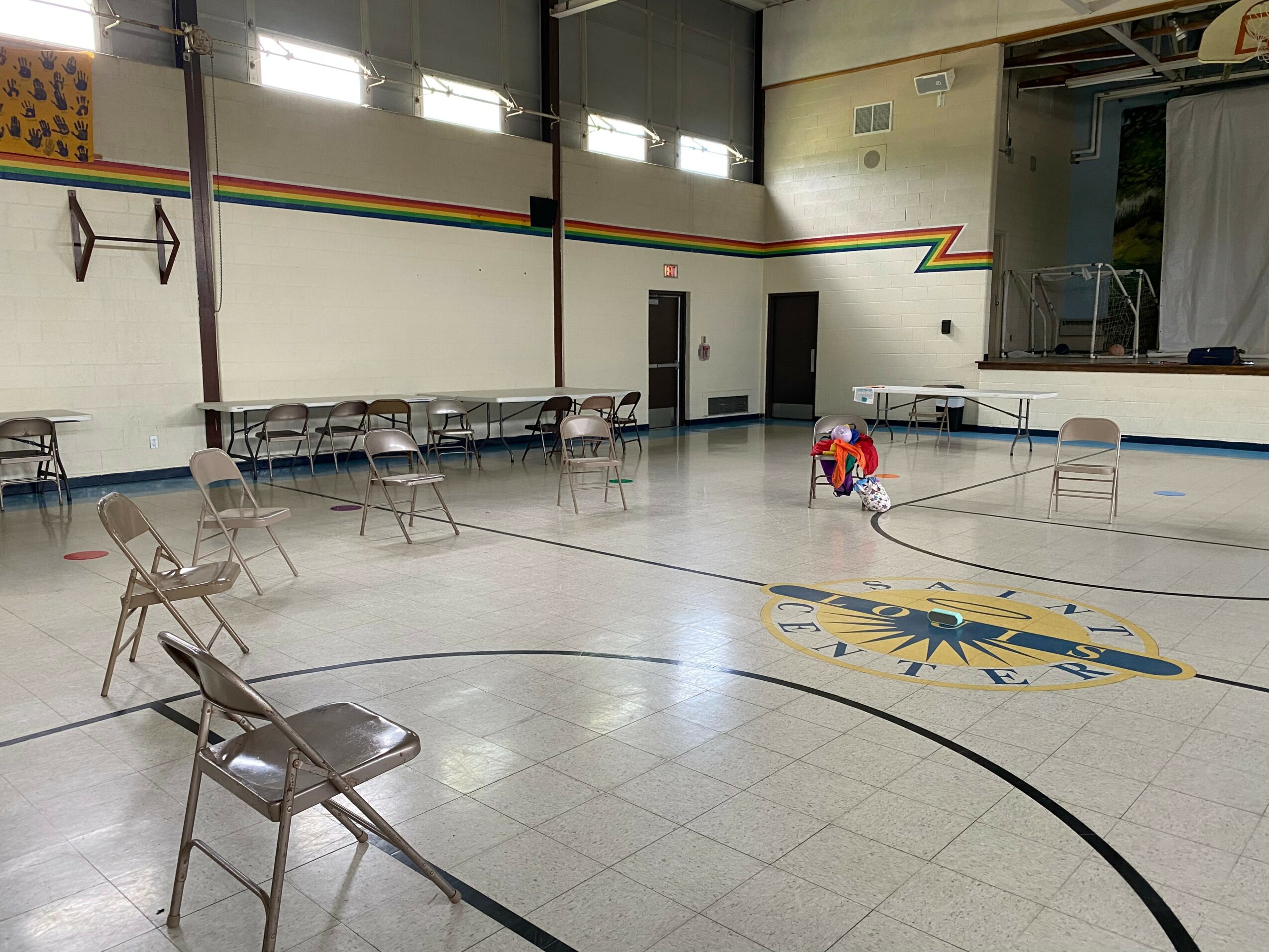 Indoor gymnasium with chairs arranged in a semi-circle, a person sitting on the floor, and a stage area in the background.