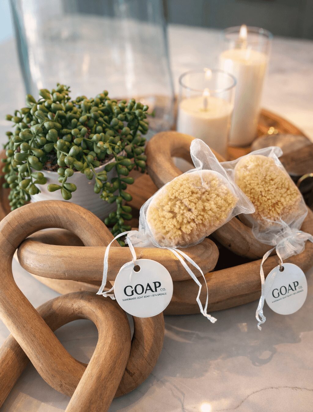 Decorative tray with two wrapped baked goods, candles, a plant, and wooden heart-shaped ornaments on a table.