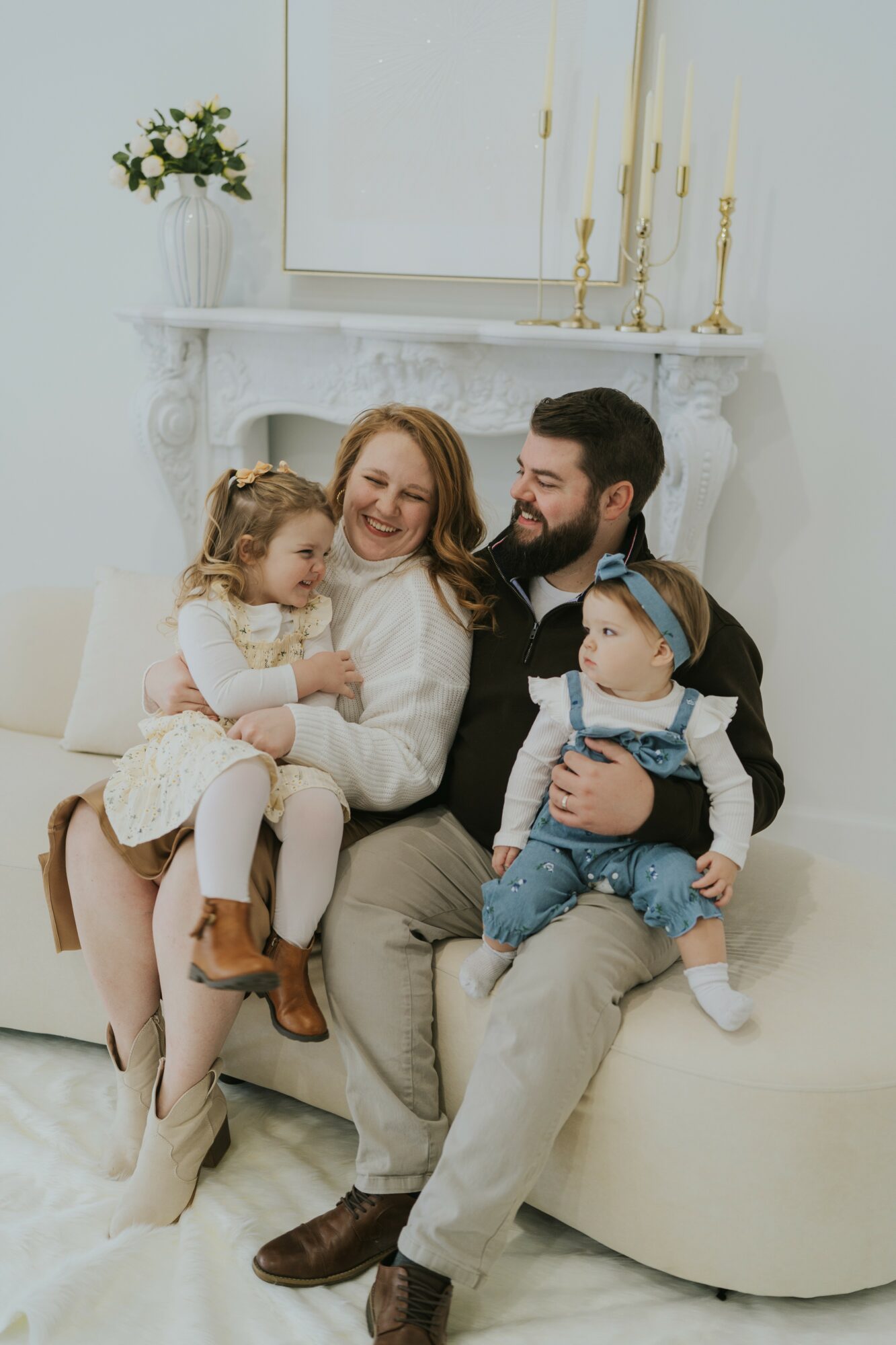 Family sitting on a sofa, smiling, with a fireplace and candles in the background.