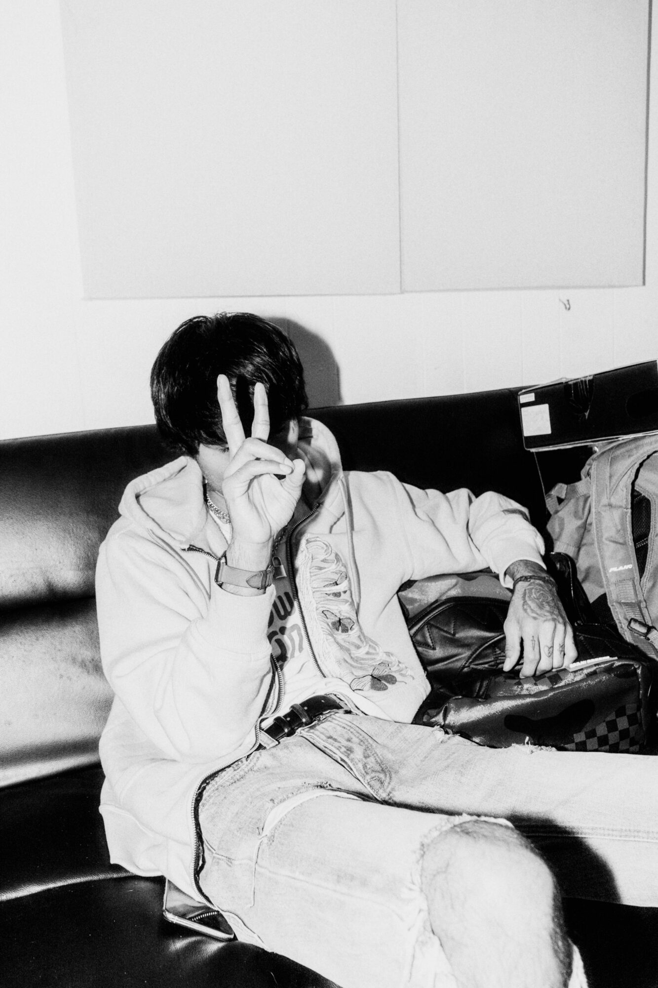 Person sitting on a couch making a peace sign with their hand, face partially covered, in black and white.