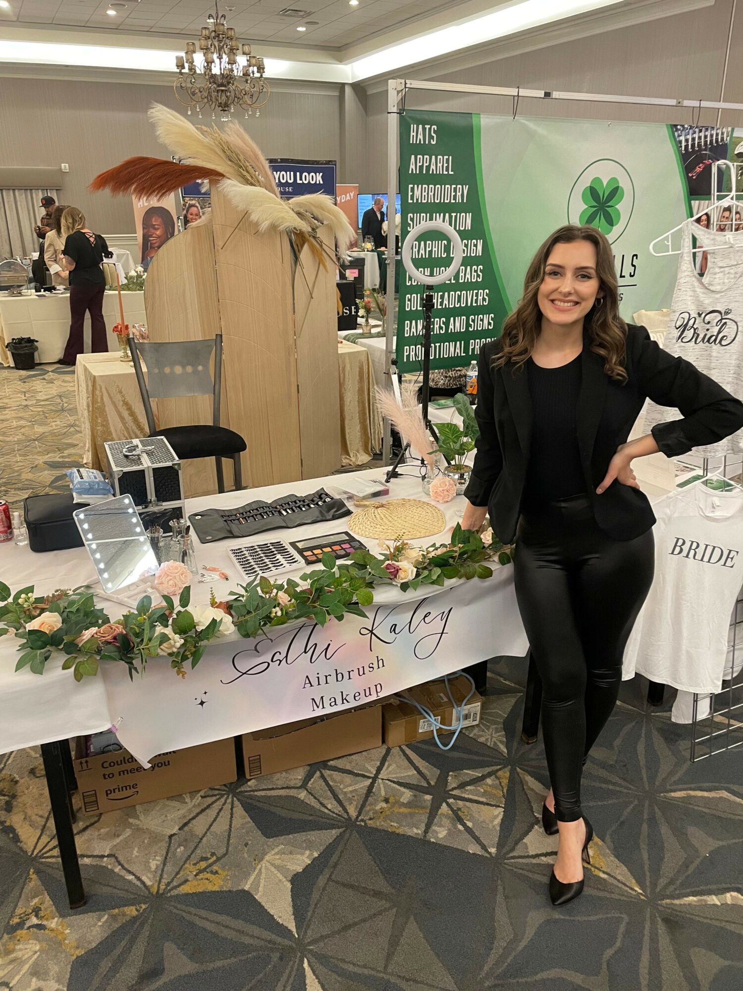 Woman standing next to a table with promotional materials and plants at an indoor event.