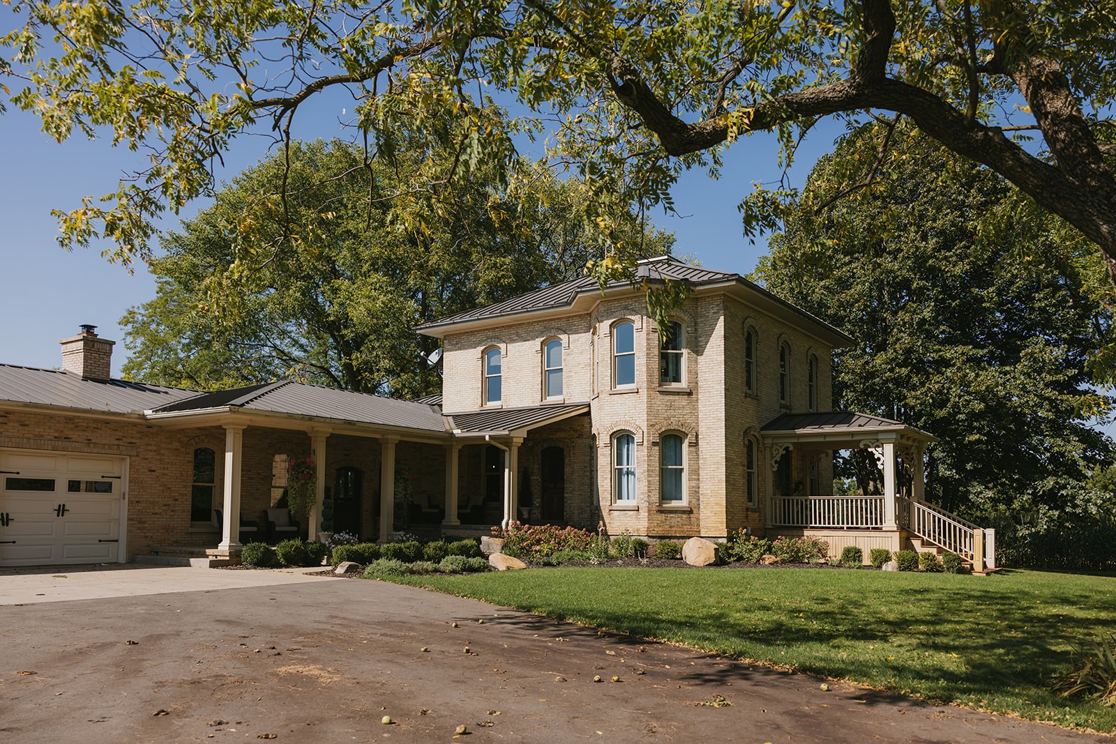 Two-story house with a porch, surrounded by trees and a lawn, under a clear blue sky.