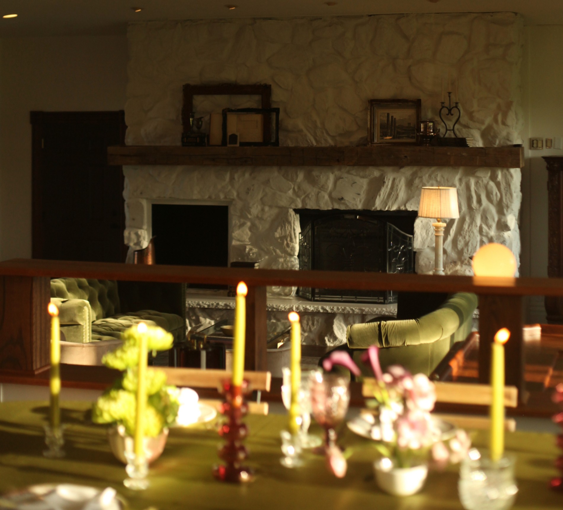 Dining table with candles and flowers, fireplace with stone wall, and shelves with decorations in background.
