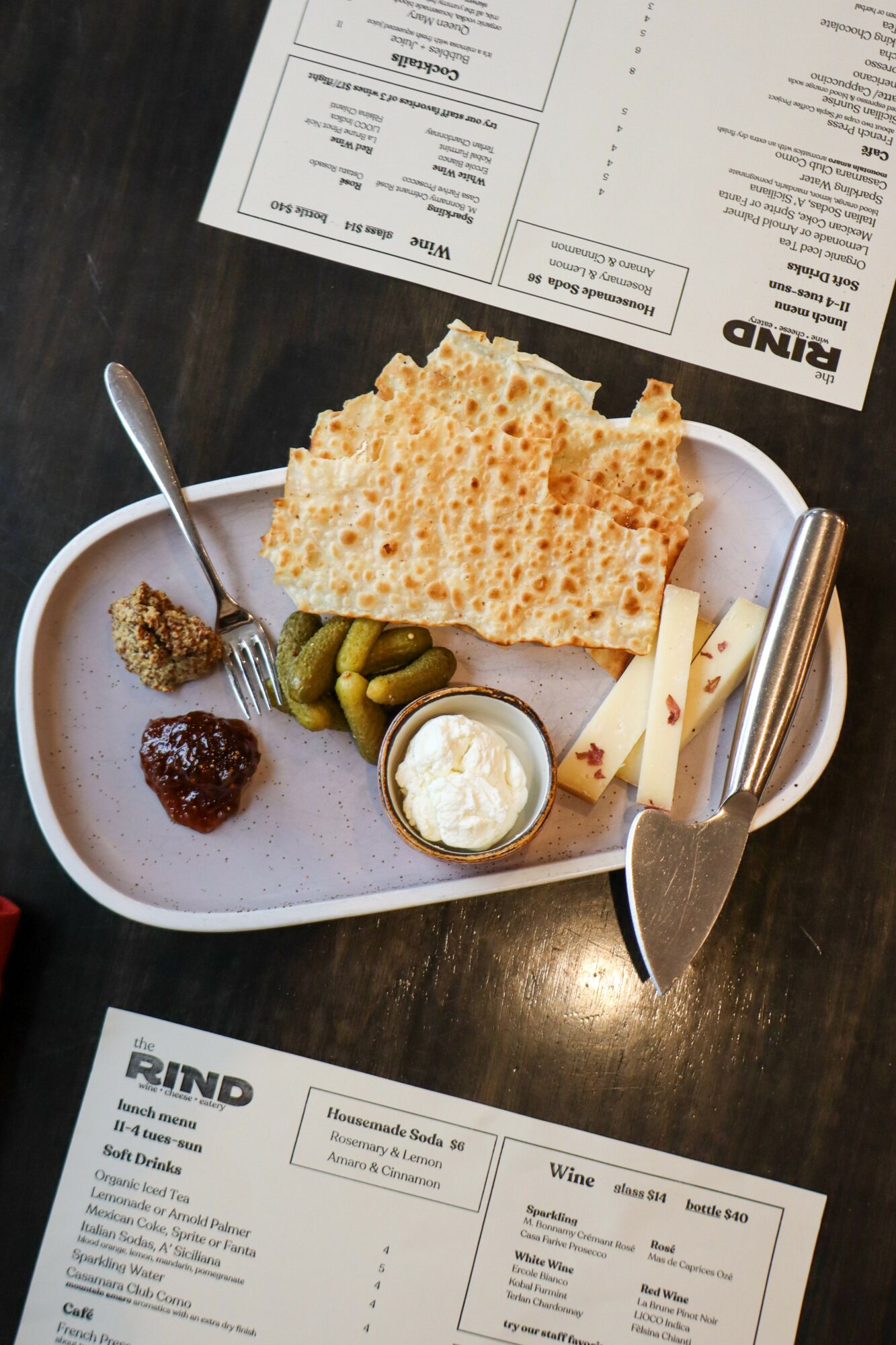 Plate with bread, pickles, cheese, butter, and condiments on a dark table, with menus nearby.