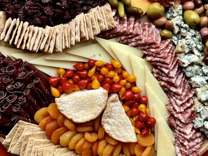 Assorted cheeses, cherry tomatoes, sliced meats, and crackers arranged on a platter.