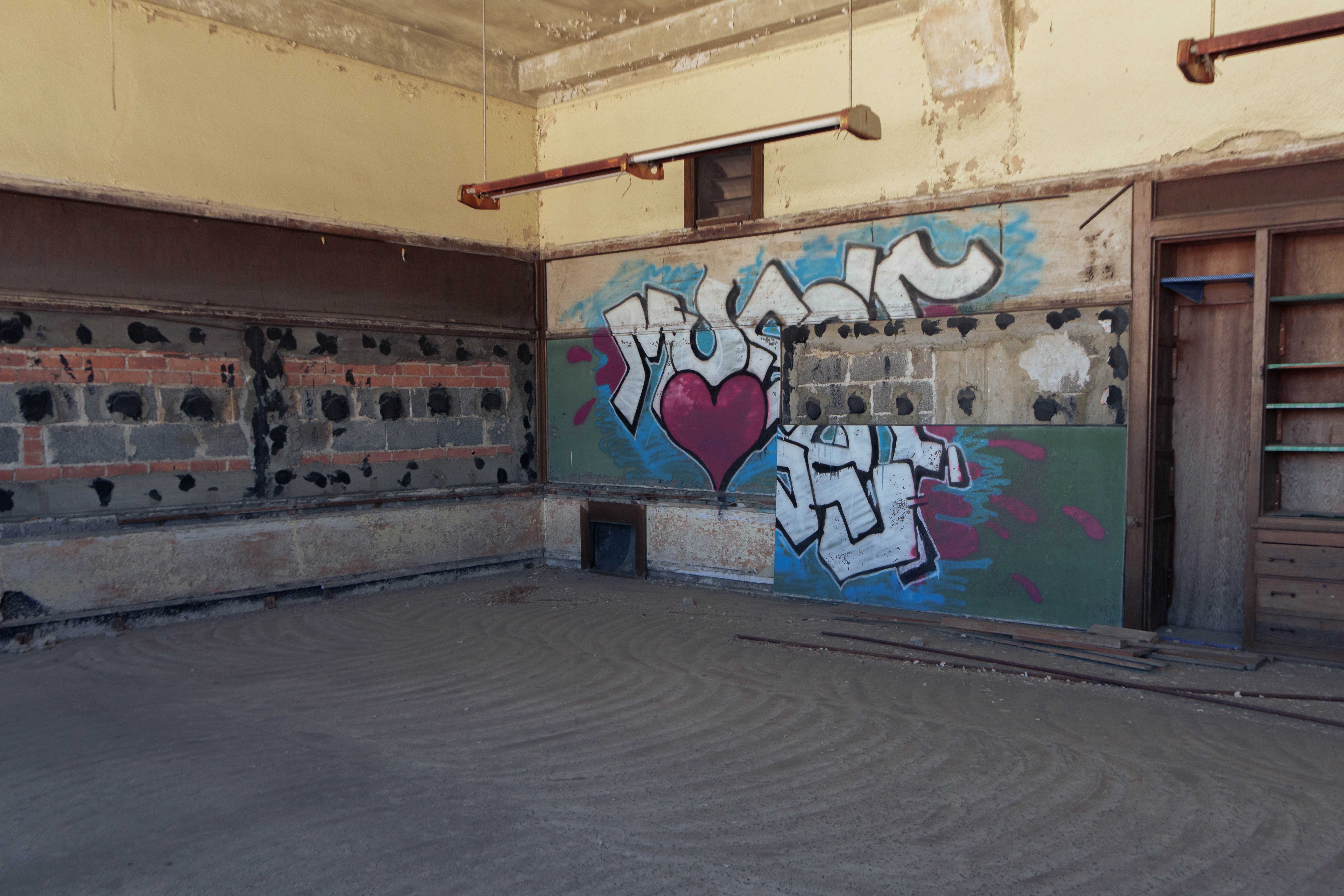 Graffiti art with a heart and abstract shapes on a wall in an urban setting, with a bench and weathered surroundings.