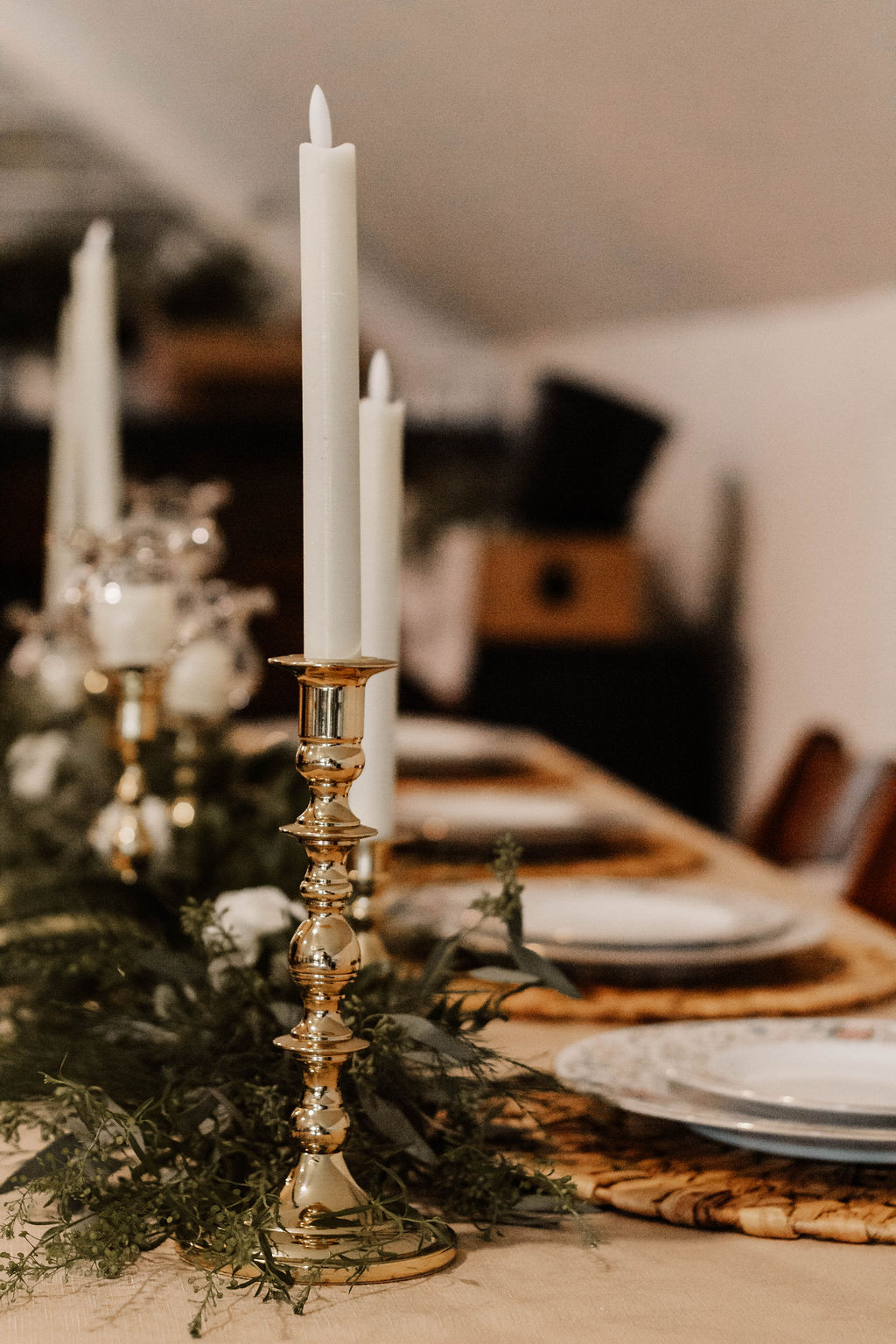 Decorative candle holder with two white candles on a festive table with greenery and tableware.