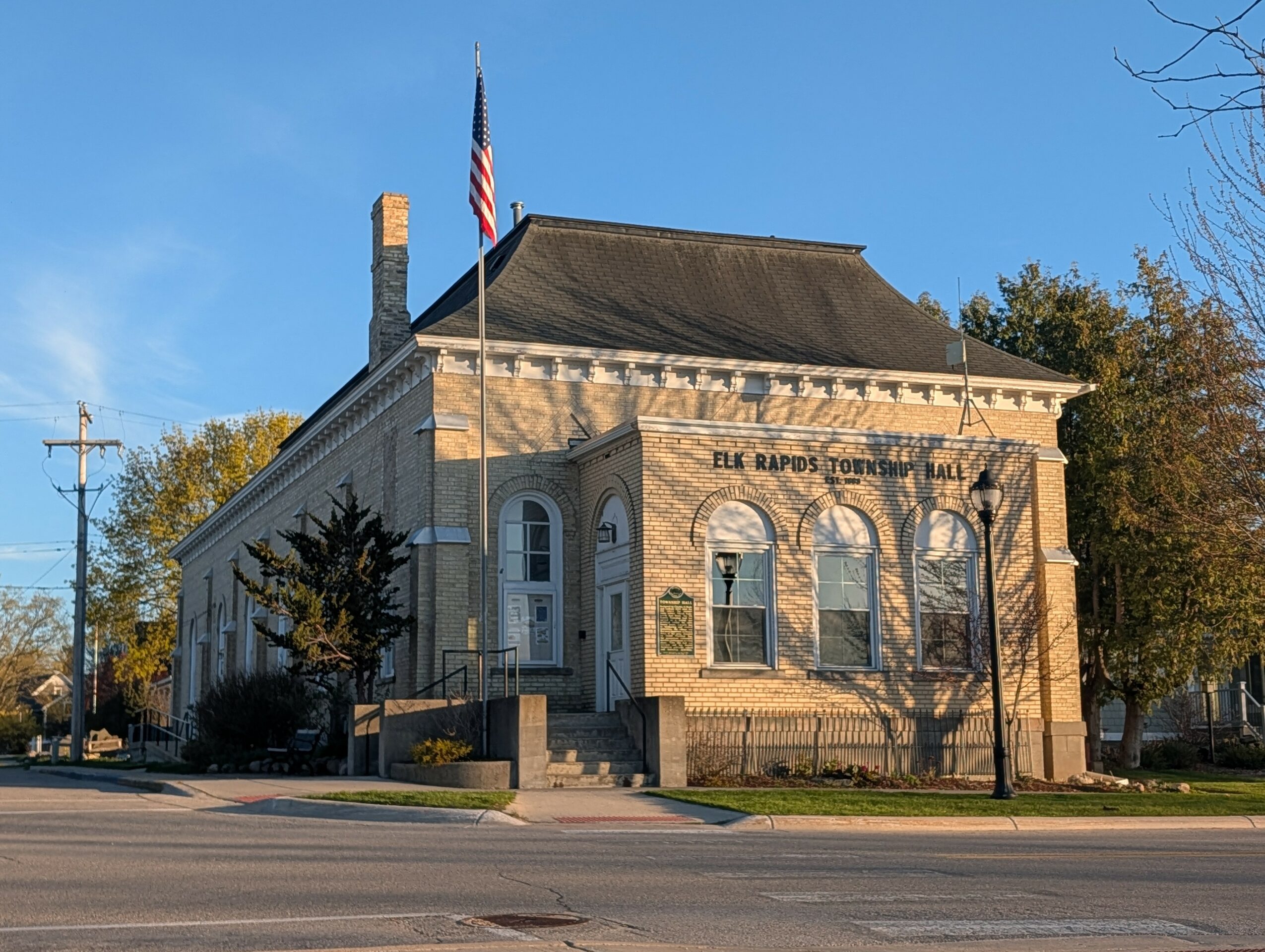 Historic building with columns and arched windows, American flag on flagpole, trees, and clear blue sky.