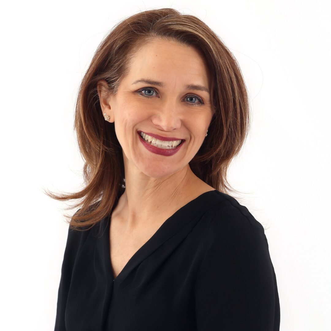 Smiling woman with shoulder-length brown hair wearing a black top, facing slightly to the right, against a white background.