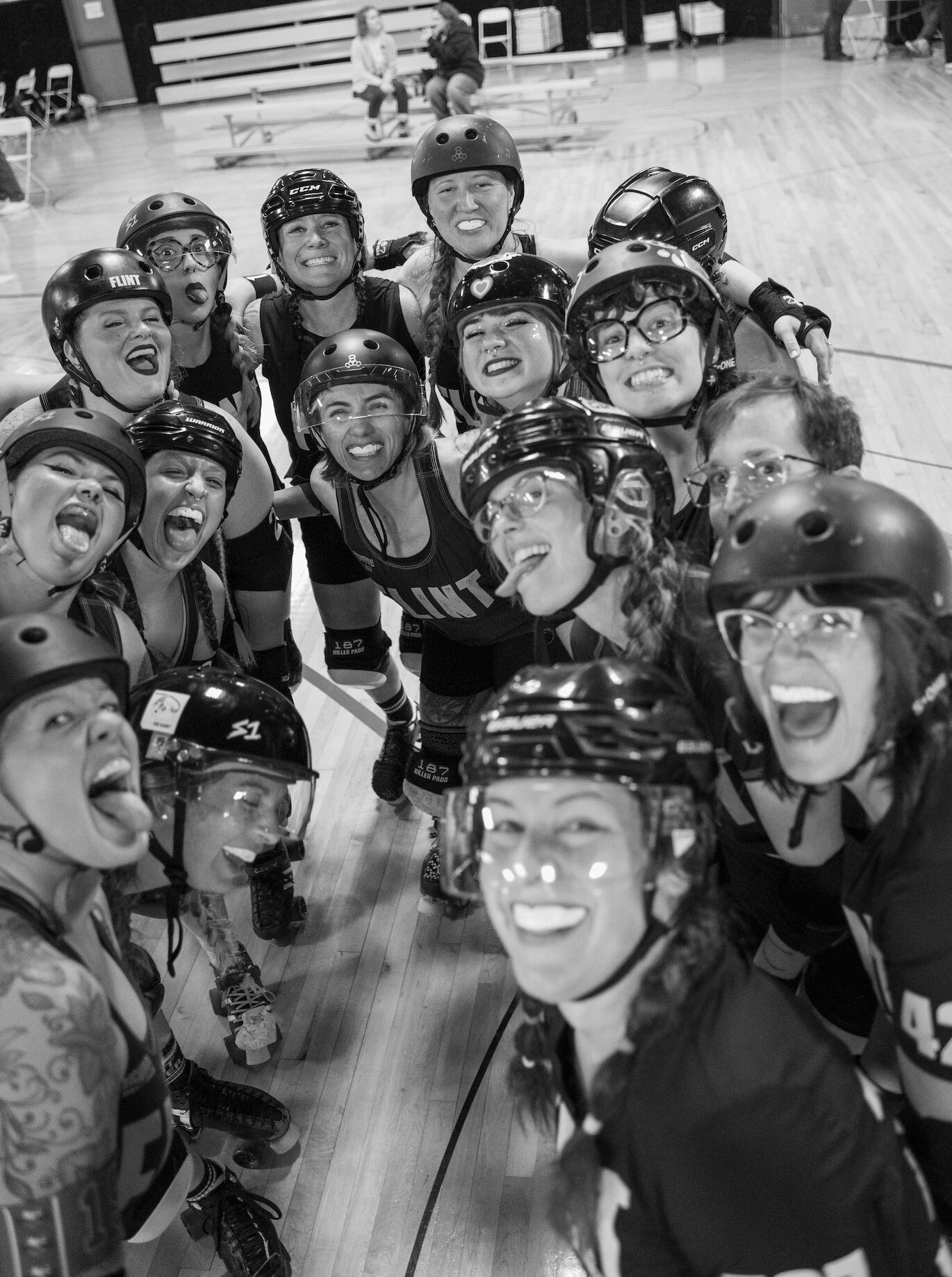 Group of people wearing helmets and protective gear, smiling and posing together indoors on a wooden floor.