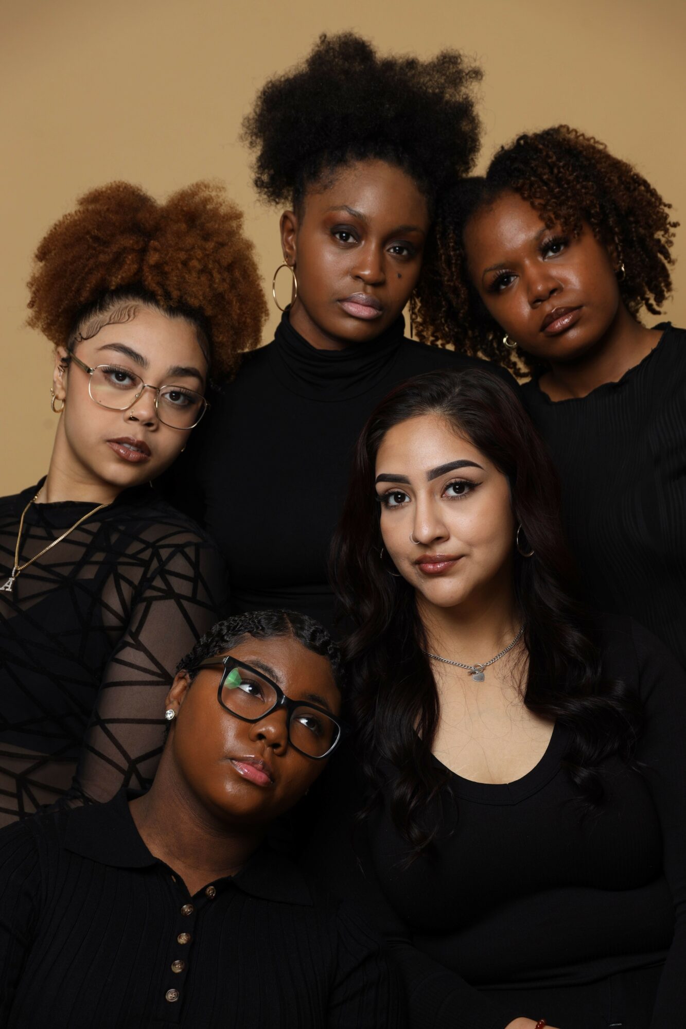 Five women with diverse hairstyles and glasses pose together indoors, smiling and looking at the camera.