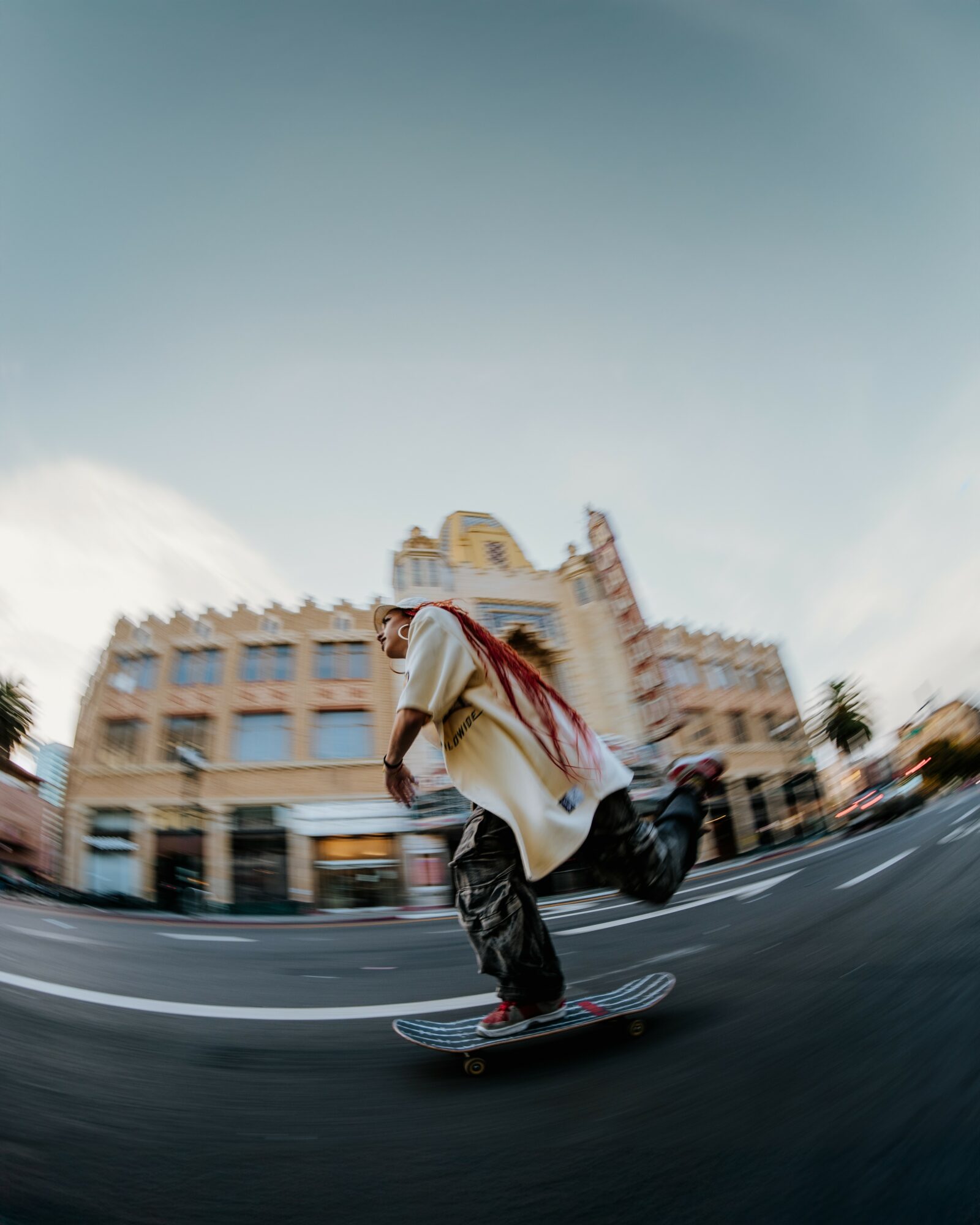 Person skateboarding on street with buildings in background, sky above, and motion blur effect.