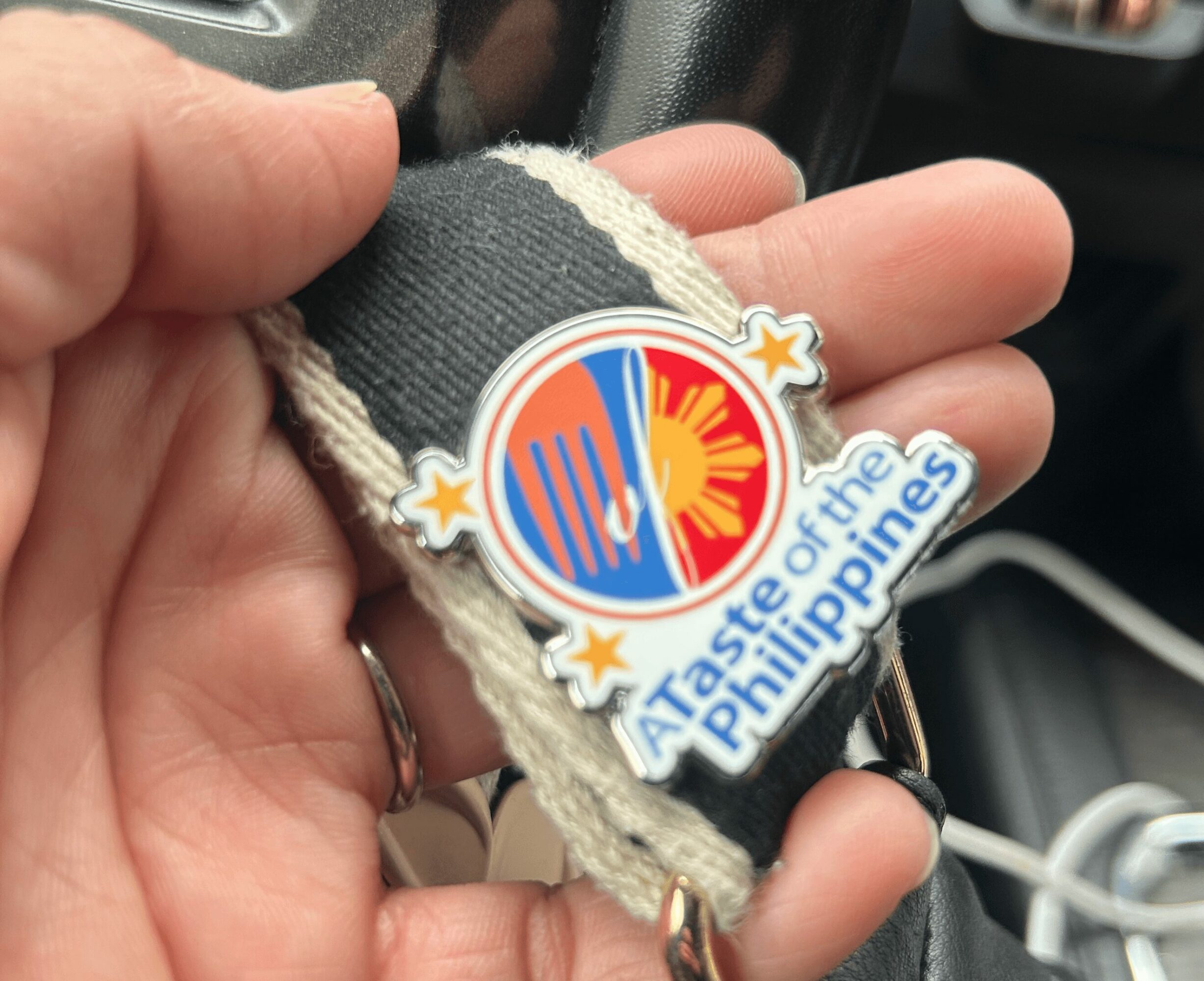 Hand holding a keychain with a sticker reading 'A Taste of the Philippines' and a colorful sun and wave design.