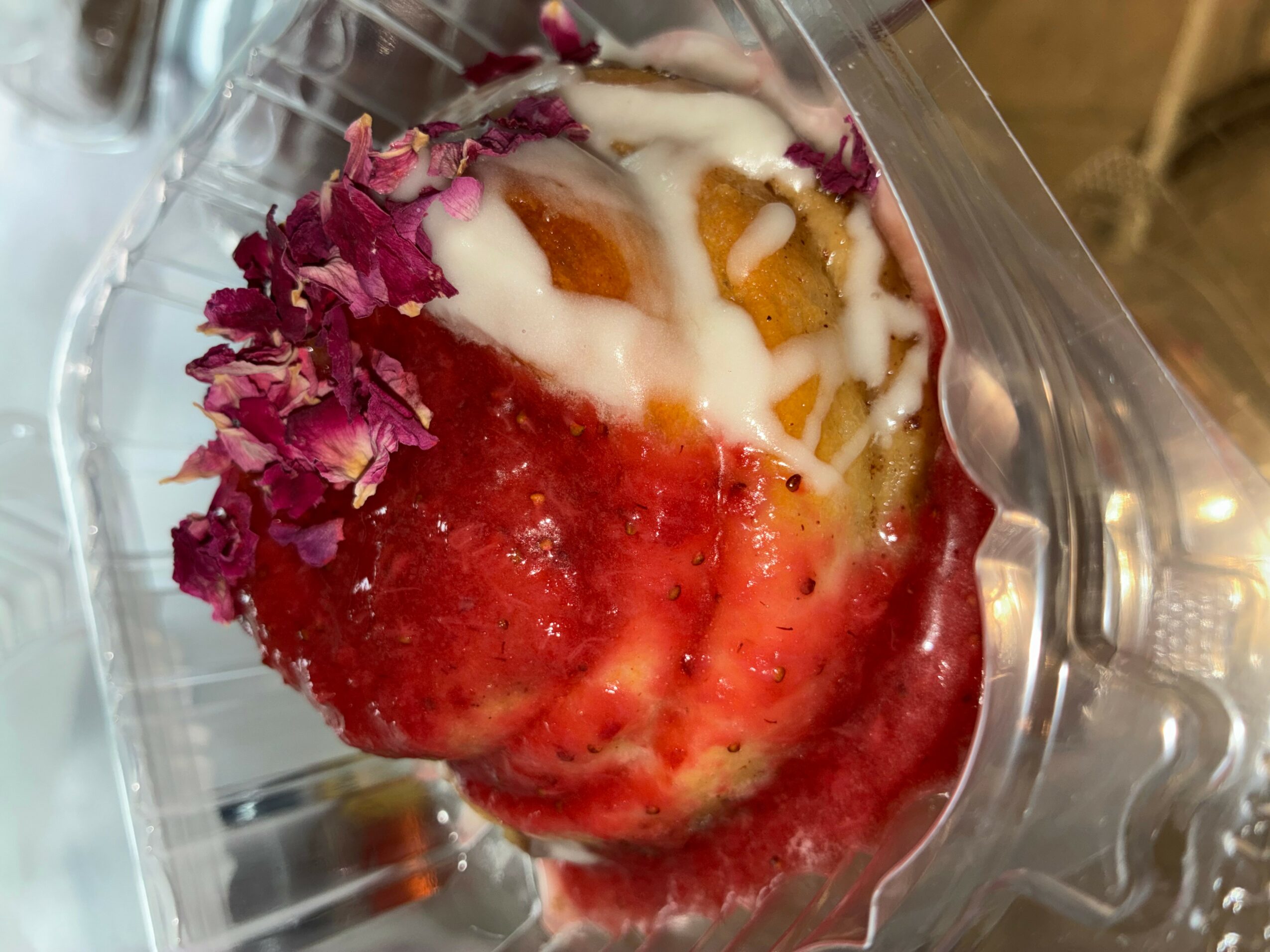 Dessert with pink flower petals, white sauce, and fruit pieces in a clear container.