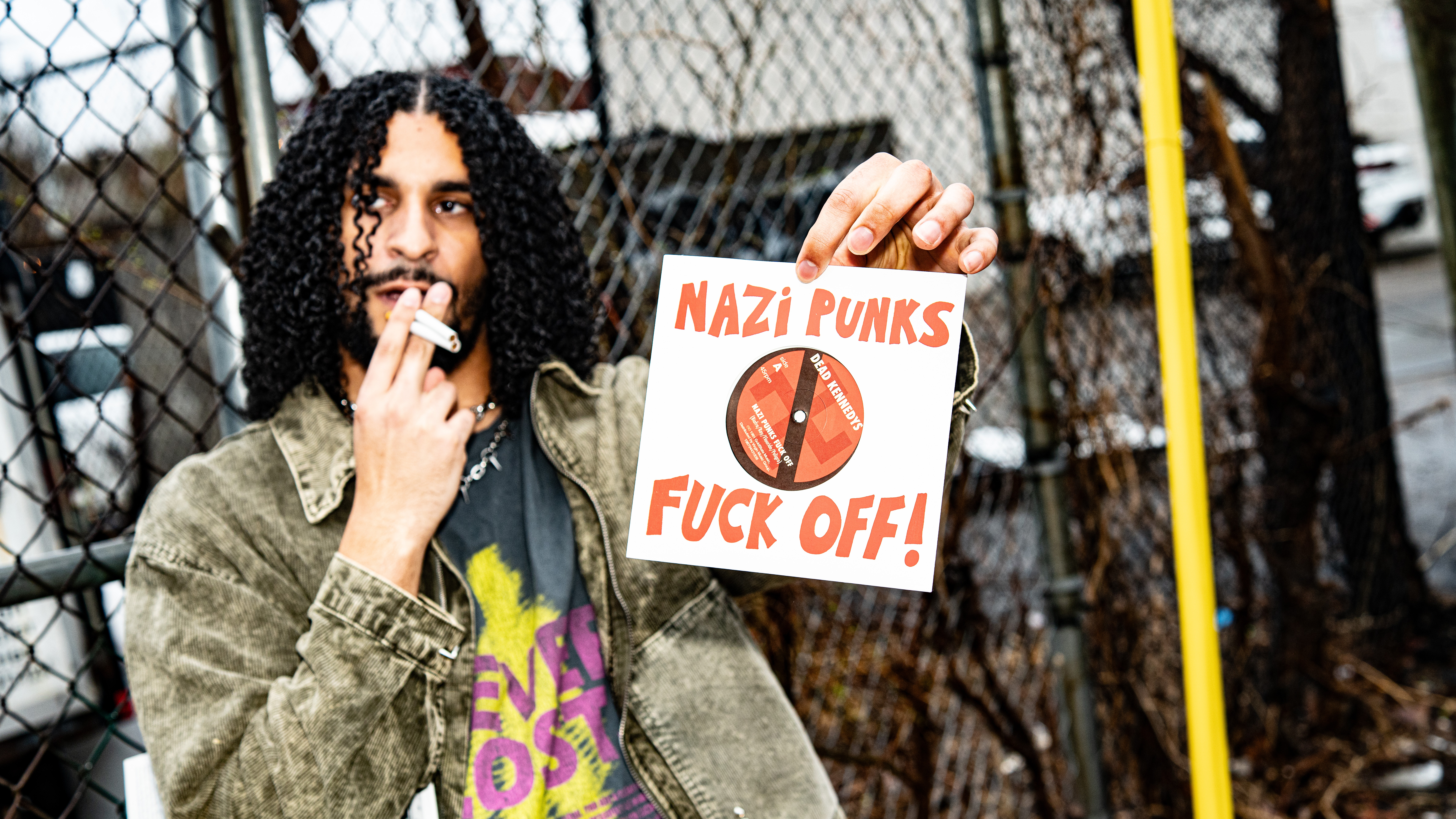 Person holding a sign that reads 'NAZI PUNKS FUCK OFF!' outdoors near a fence.