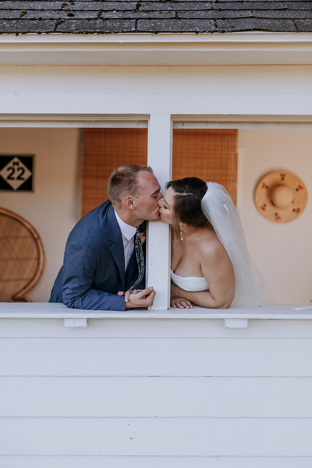 Bride and groom kiss through a window, with wedding attire and a white background, celebrating their wedding day.