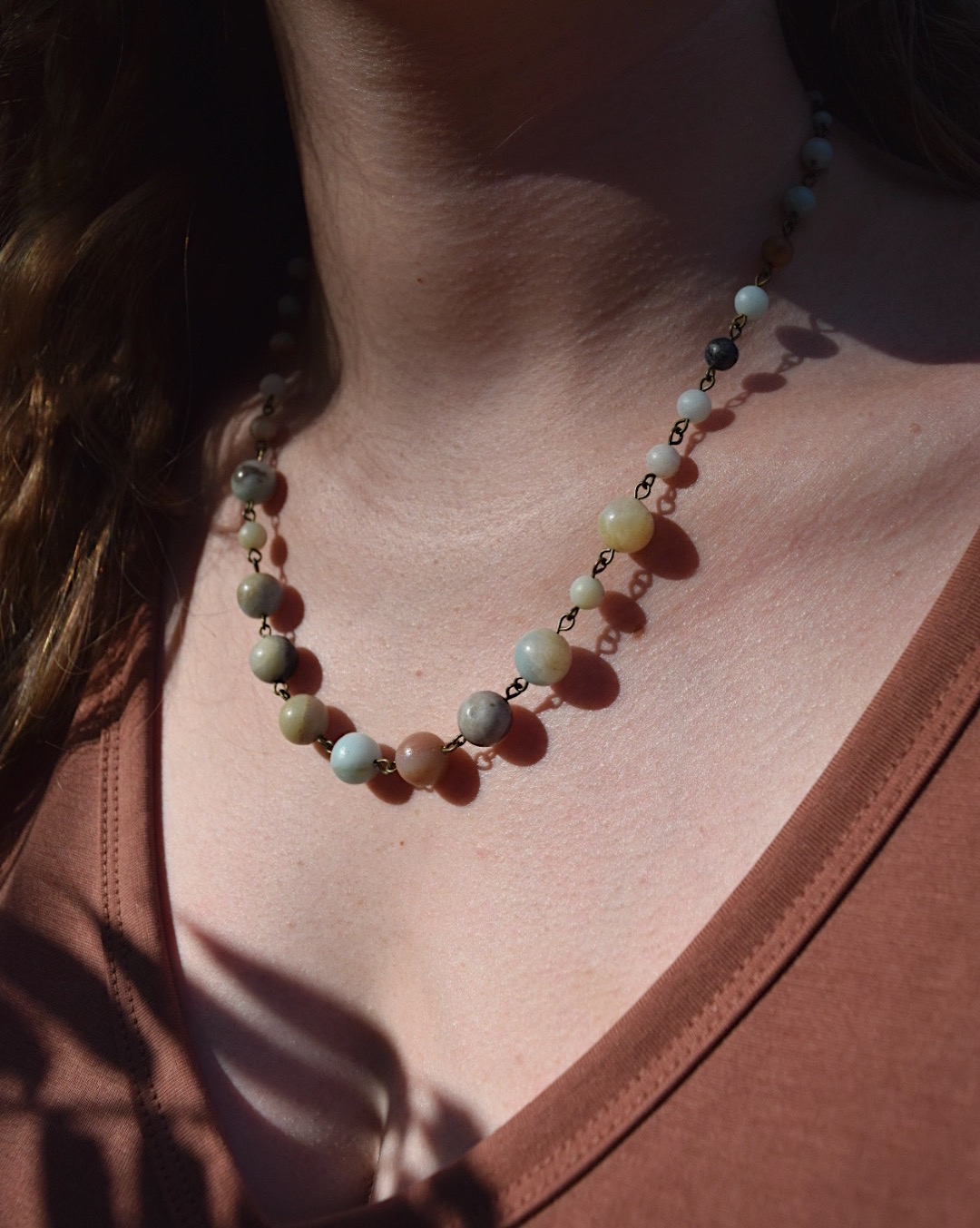Close-up of a person's neck and chest wearing a colorful beaded necklace, with sunlight casting shadows.