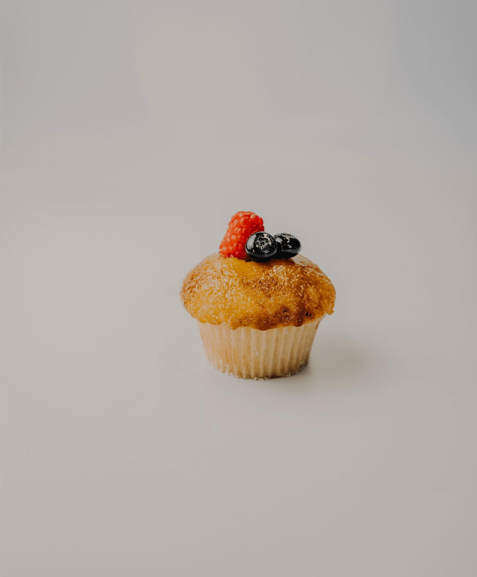 Cupcake topped with berries on a plain background.