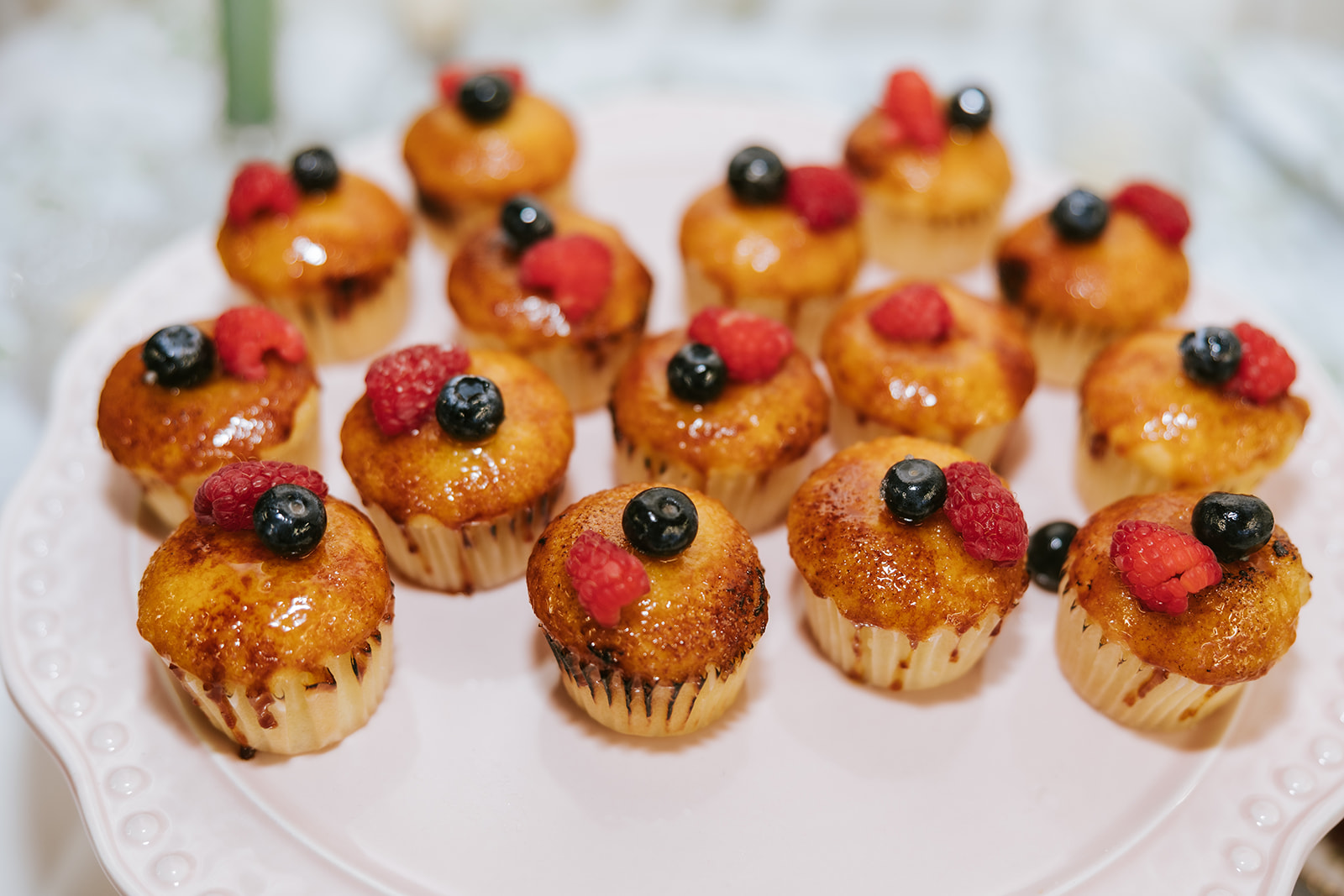 Small cupcakes topped with berries arranged on a white plate, with a blurred background.