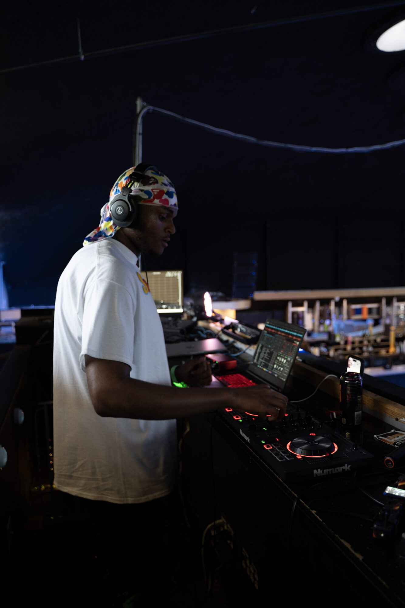 DJ wearing headphones and a white shirt operating DJ equipment in a dark room.